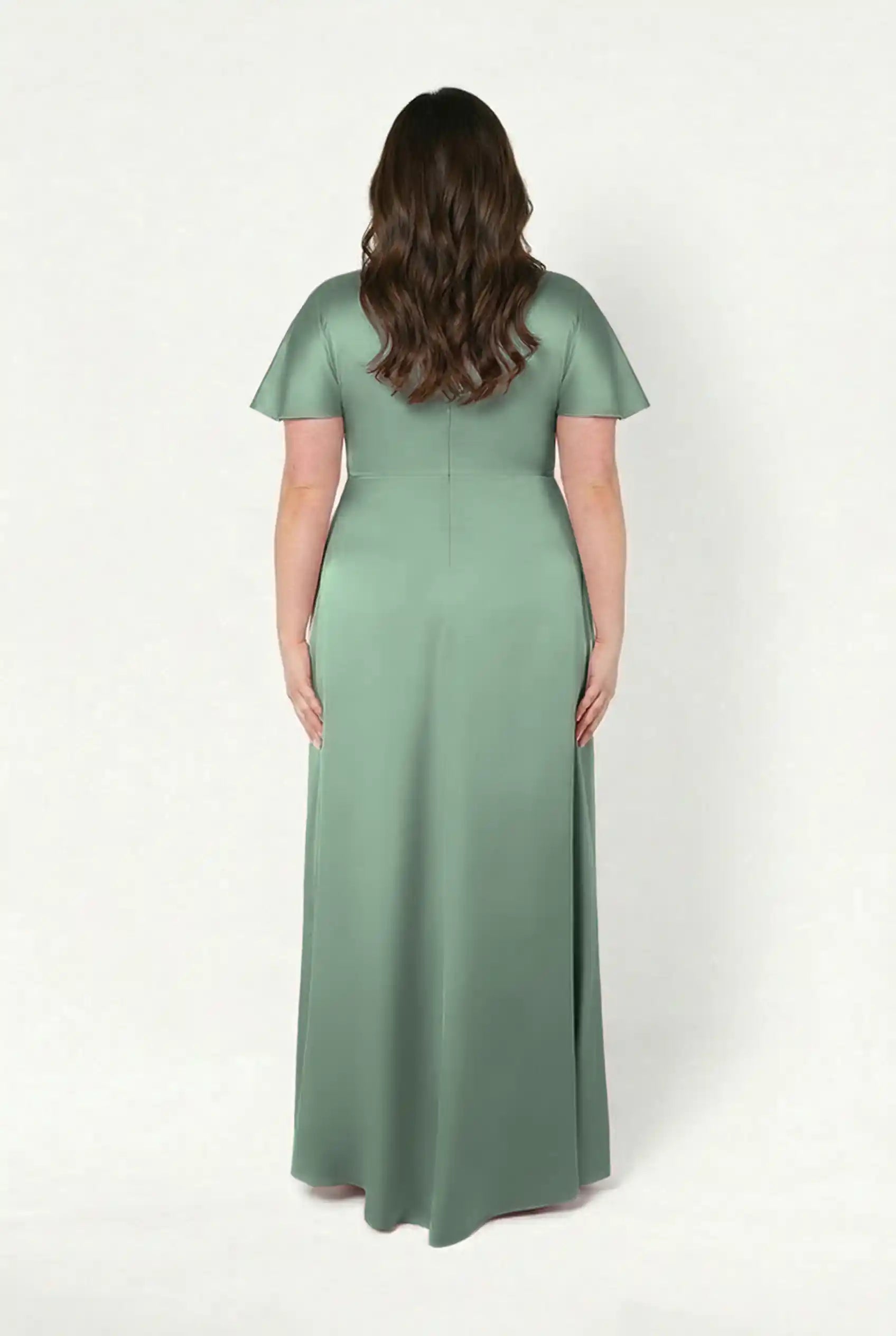 A woman with long brown hair, seen from behind, wears the floor-length TH&TH Camilla Bridesmaid Dress in Sage Green Satin, featuring short sleeves and a fitted waist, standing against a plain white background.