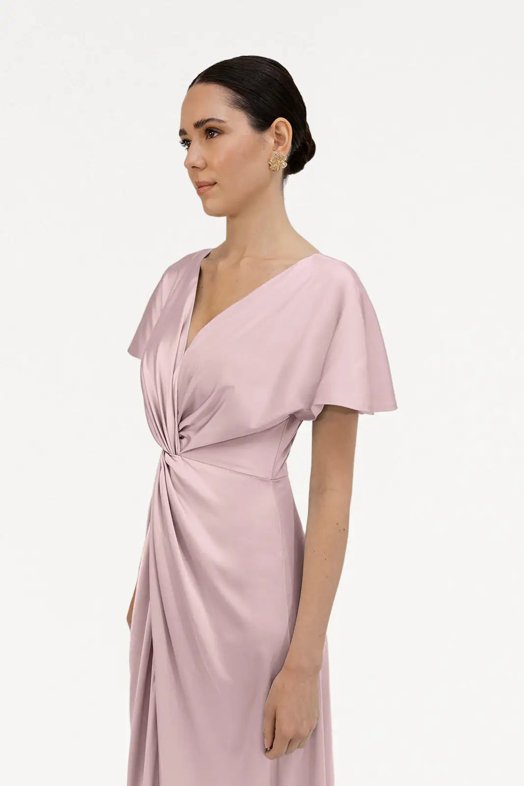 A woman with dark hair in a low bun wears the TH&TH Camilla Bridesmaid Dress in Smoked Blush Satin, a short-sleeved V-neck style with a waist twist detail. She stands against a plain white background, facing slightly left.
