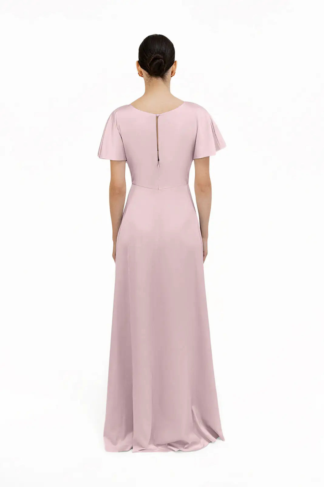A woman stands with her back to the camera, wearing the Camilla Bridesmaid Dress in Smoked Blush Satin by TH&TH—a floor-length, short-sleeved gown with a modest neckline and fitted waist—against a plain white background.