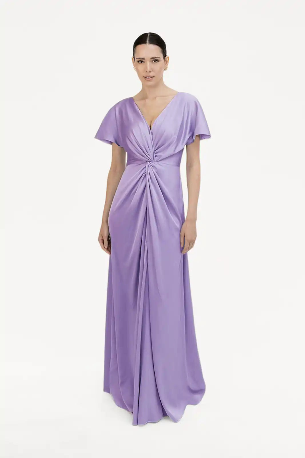 A woman models the size-inclusive TH&TH Camilla Bridesmaid Dress in violet satin—a floor-length, short-sleeved gown with V-neckline and twist-knot bodice—set against a plain white background.