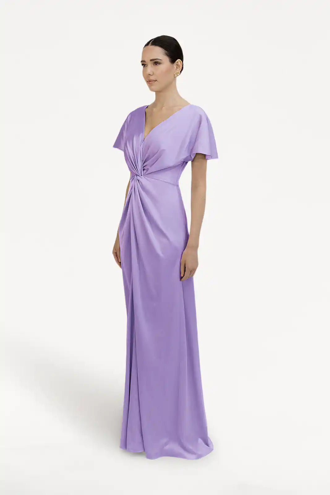 A woman models the TH&TH Camilla Bridesmaid Dress in Violet Satin, a floor-length, size-inclusive gown with a twist-knot bodice and V-neckline. Her hair is neatly pulled back as she poses against a white background.
