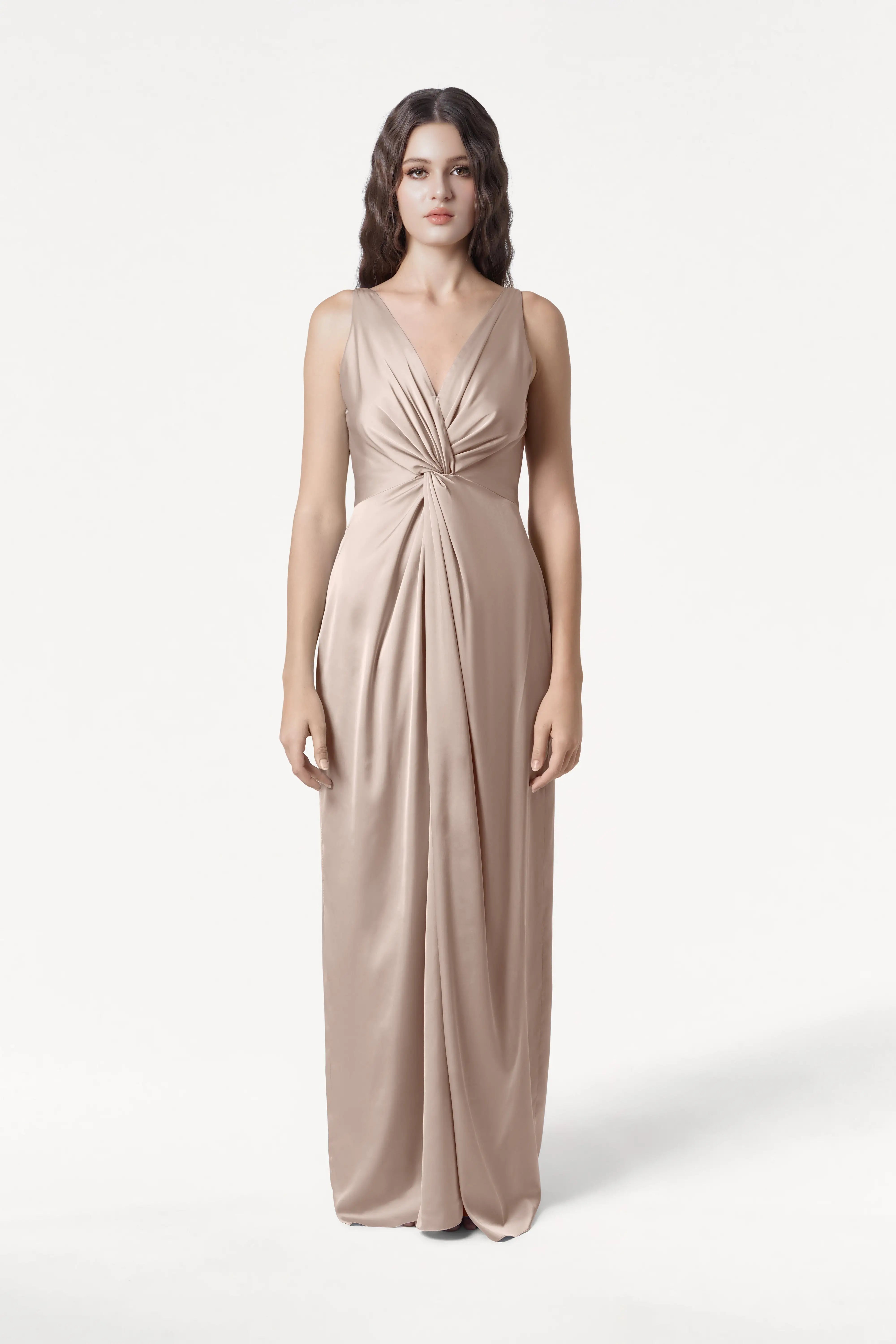 A woman with long wavy hair wears the TH&TH Carmen Bridesmaid Dress in Champagne Sky Satin—a sleeveless, floor-length gown with a deep V-neck and gathered waist—ideal for modern bridal parties seeking a flattering look.