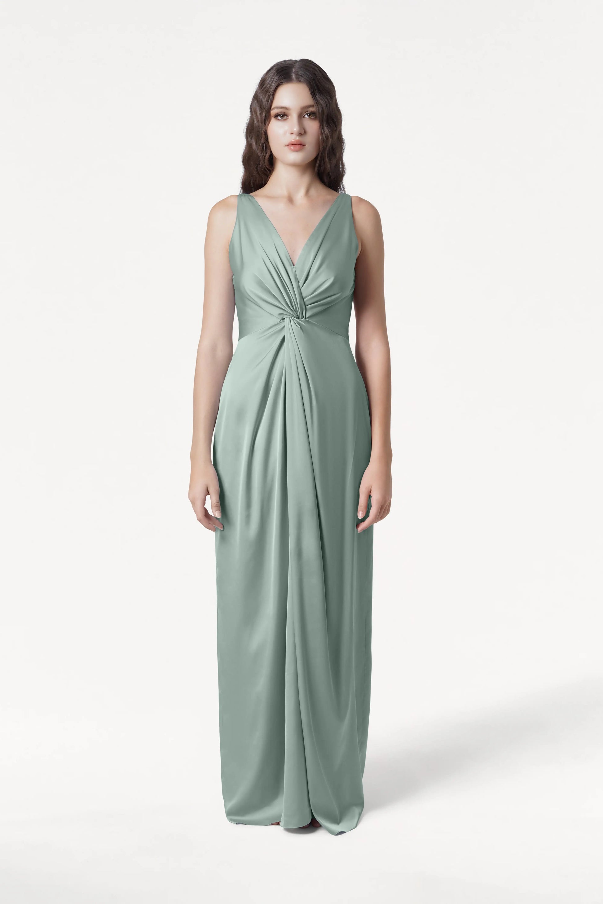 A woman faces forward in the TH&TH Carmen Bridesmaid Dress, a sleeveless, floor-length gown in dusty eucalyptus satin with a deep V-neck and gathered waist detail, set against a plain white background.