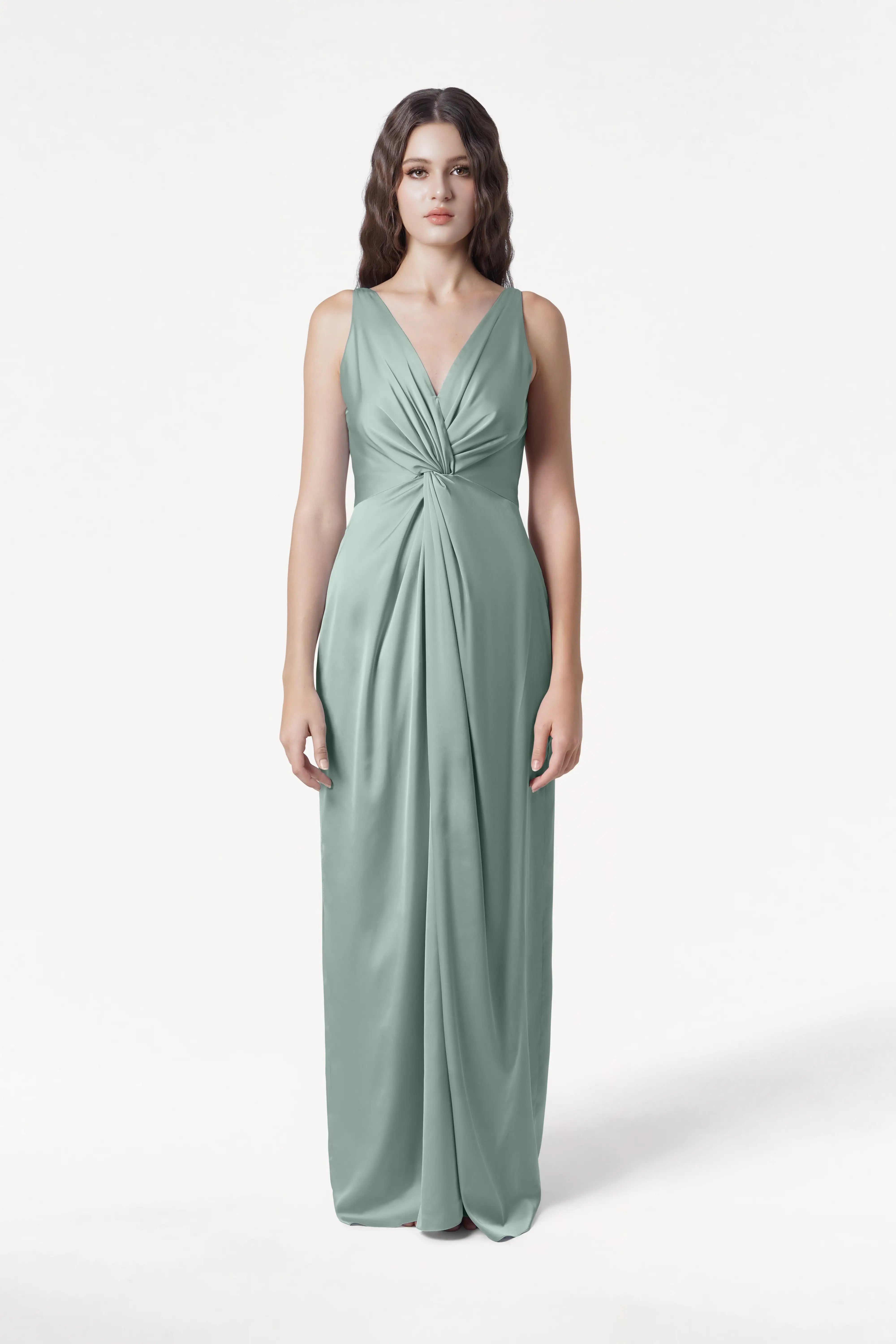 A woman faces forward in the TH&TH Carmen Bridesmaid Dress, a sleeveless, floor-length gown in dusty eucalyptus satin with a deep V-neck and gathered waist detail, set against a plain white background.