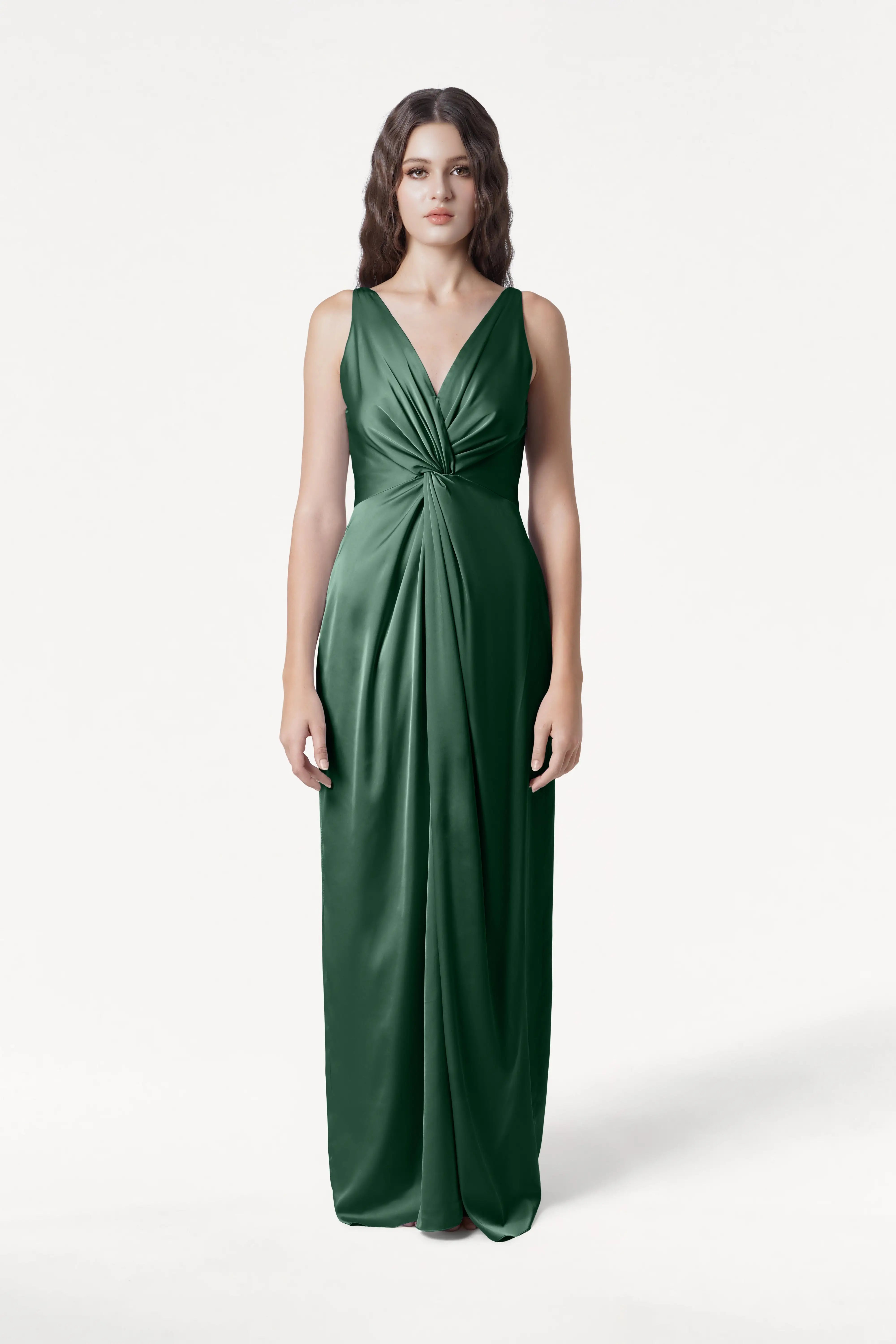 A woman stands against a white background wearing the TH&TH Carmen Bridesmaid Dress in Olive Grove Satin, a sleeveless, floor-length gown with a V-neckline and twist-knot waist—an elegant look for modern bridal parties.