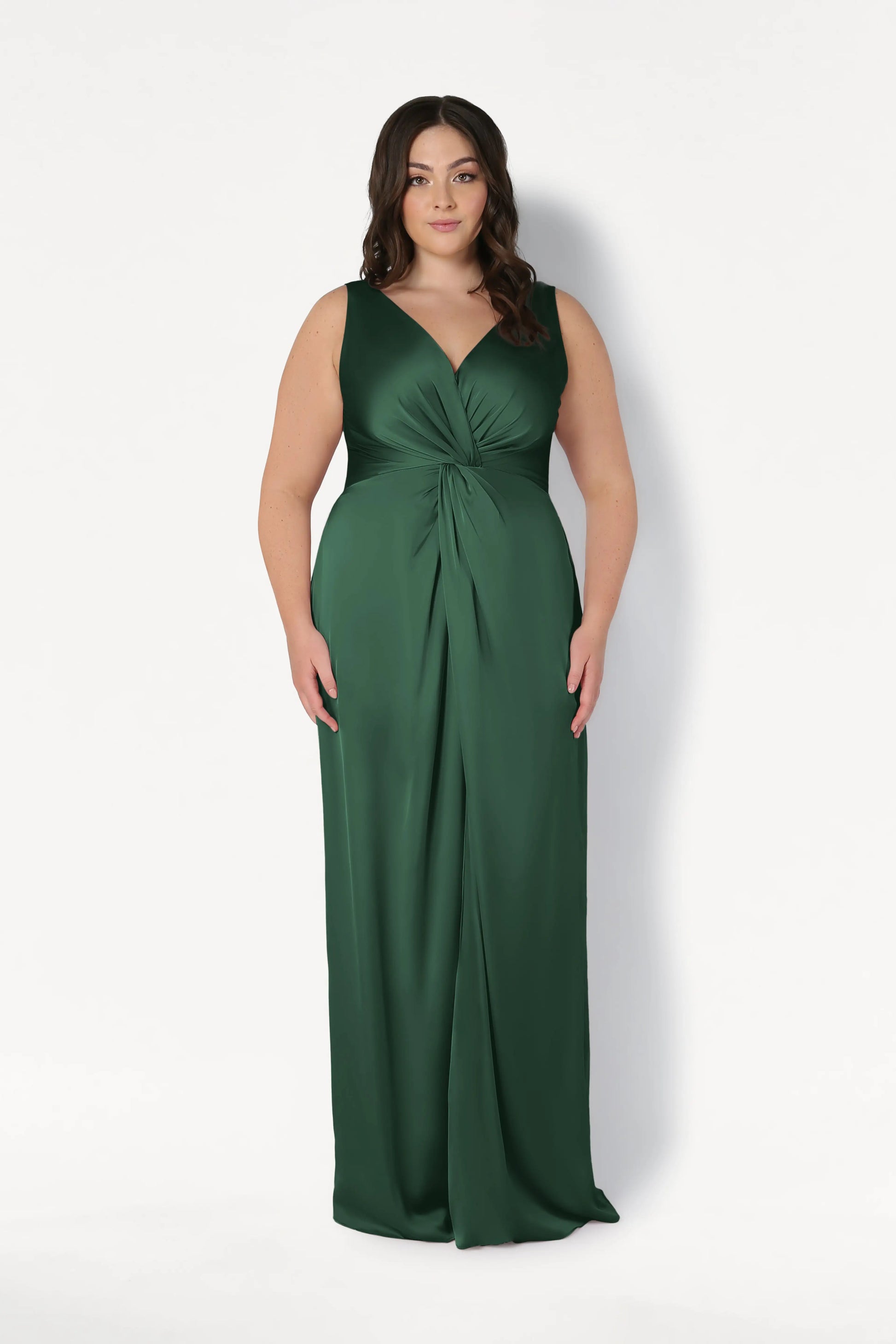 A woman with long, dark hair wears the TH&TH Carmen Bridesmaid Dress in Olive Grove Satin—a sleeveless, floor-length gown with a deep V-neck and twist-knot waist—standing against a plain white background, facing forward.