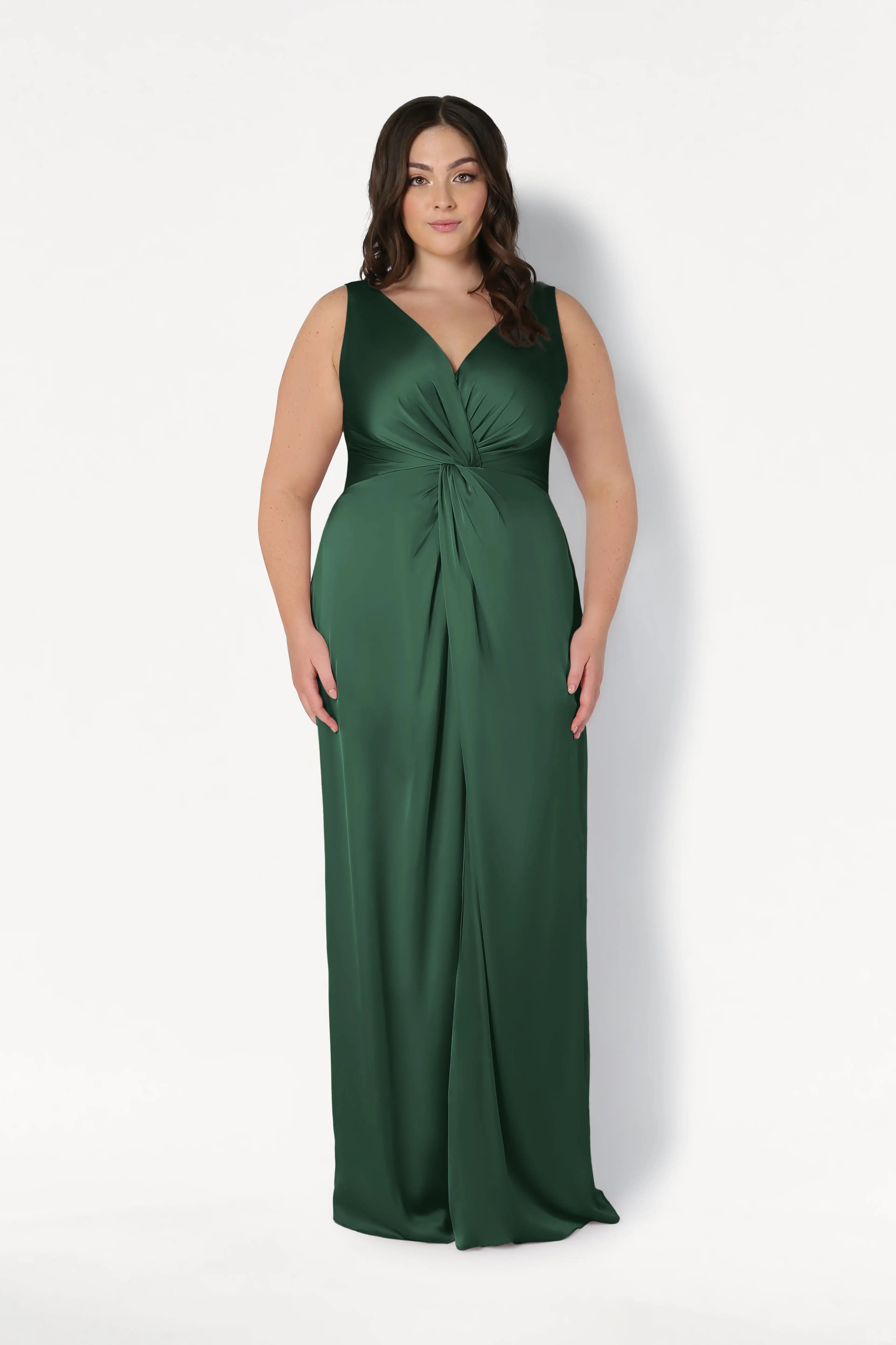 A woman with long, dark hair wears the TH&TH Carmen Bridesmaid Dress in Olive Grove Satin—a sleeveless, floor-length gown with a deep V-neck and twist-knot waist—standing against a plain white background, facing forward.