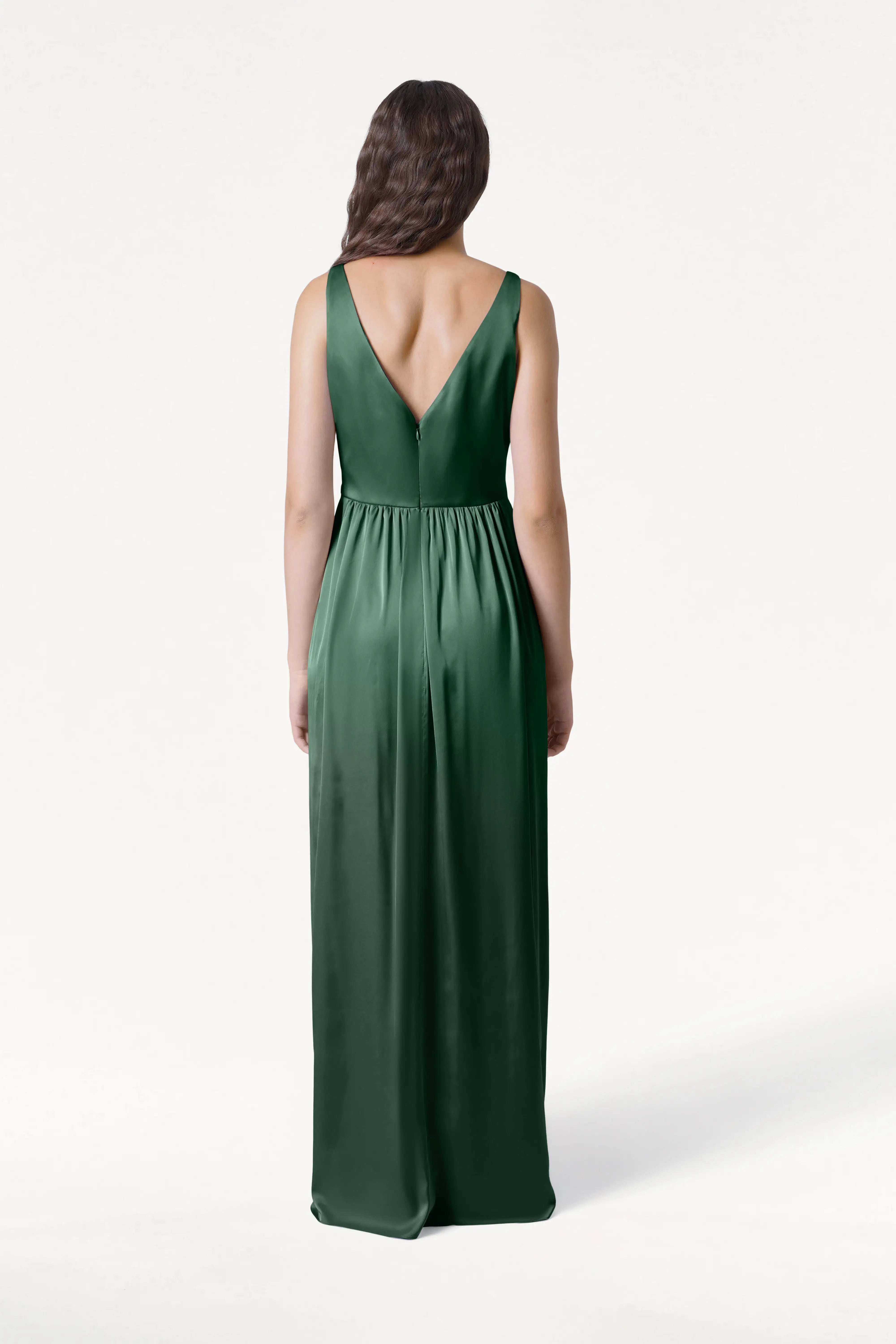 A woman with long, wavy brown hair faces away, modeling the TH&TH Carmen Bridesmaid Dress in Olive Grove Satin—a sleeveless, floor-length gown with a V-shaped back—ideal for modern bridal parties against a plain white background.