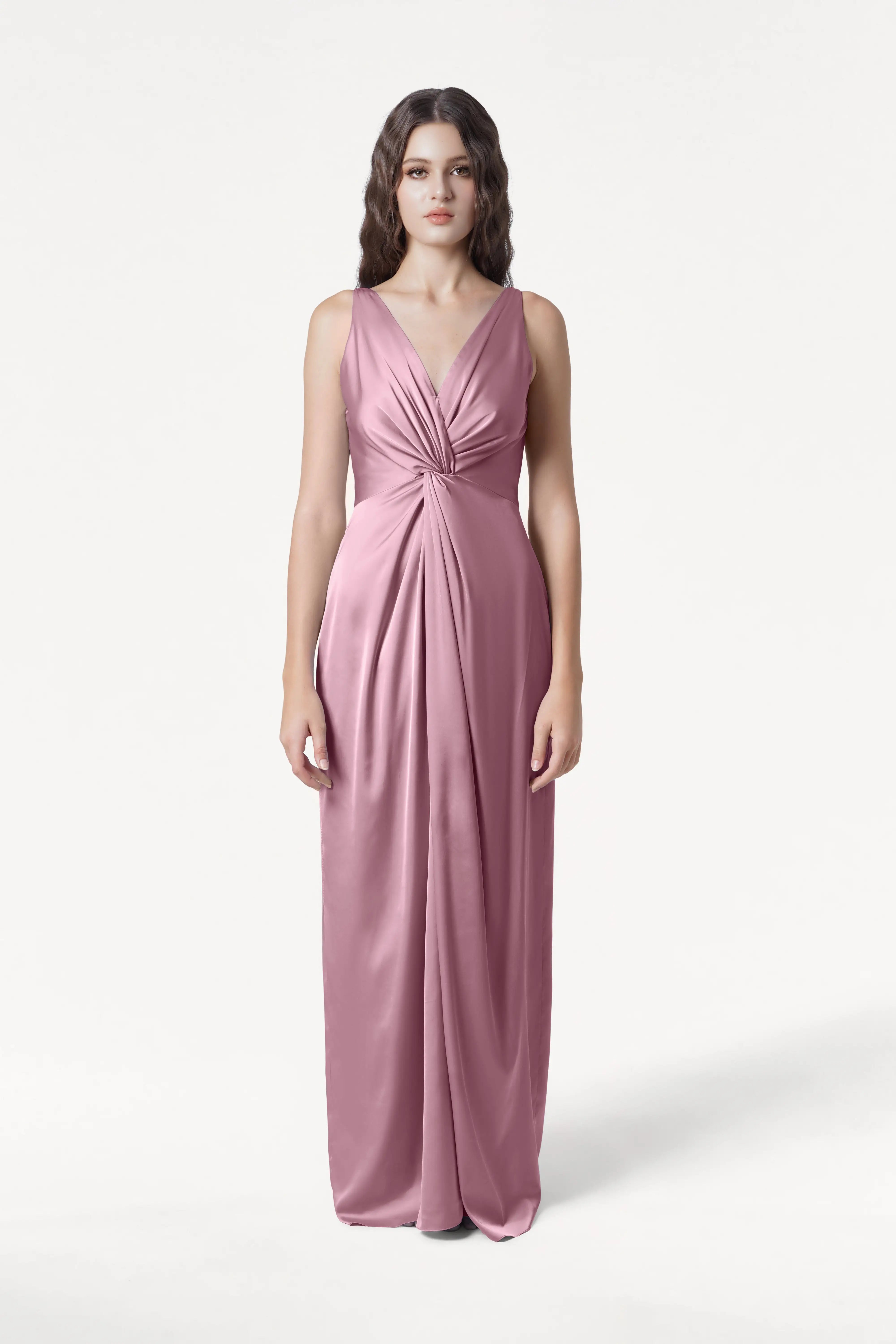 A woman faces forward in the TH&TH Carmen Bridesmaid Dress, a sleeveless, floor-length satin gown in rose pink with a twist-knot waist and soft drape. Shown on a plain white background. Ideal as a modern bridal party dress.