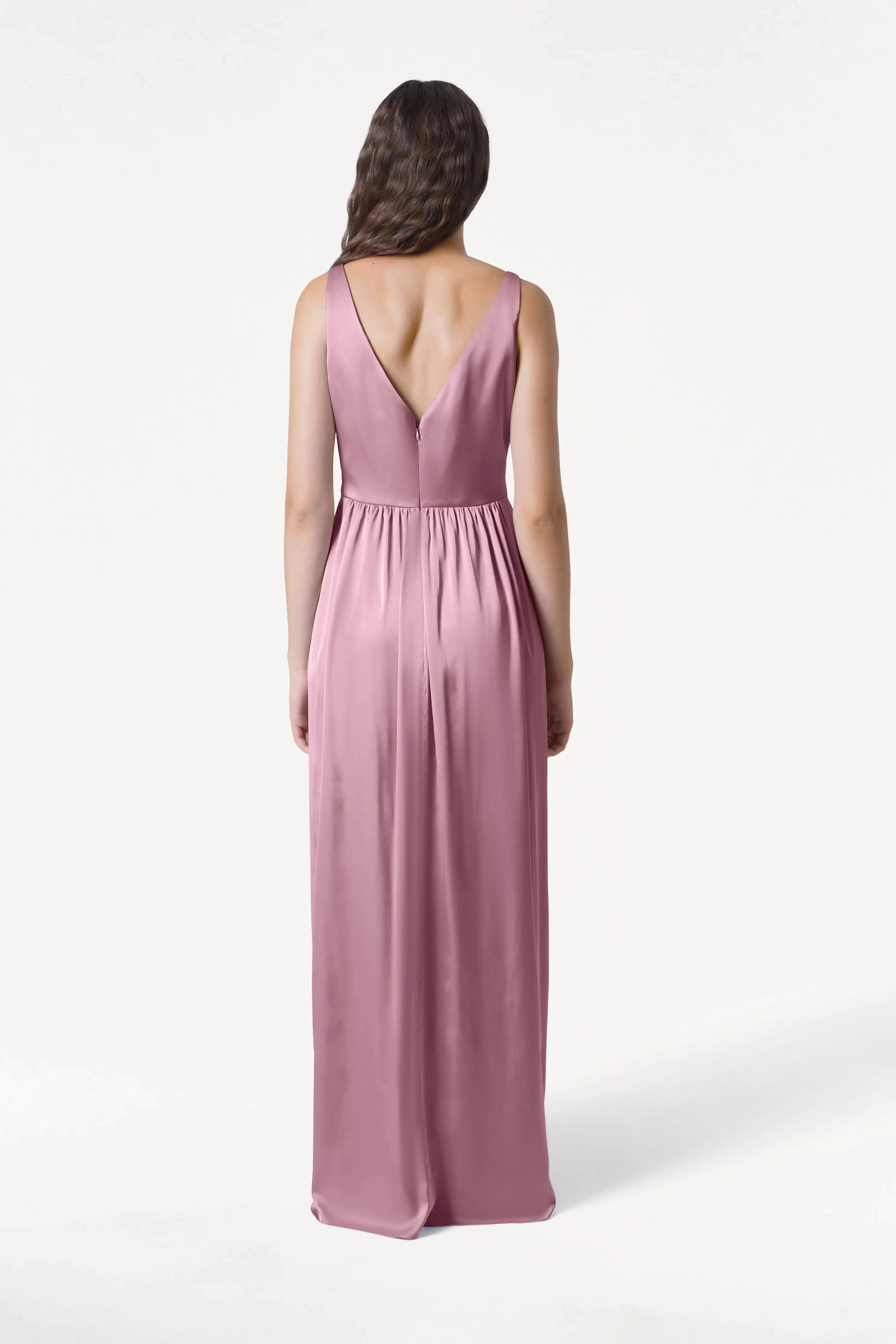 A woman with loose waves faces away in the TH&TH Carmen Bridesmaid Dress, featuring rose pink satin and a deep V-back, set against a plain white background.