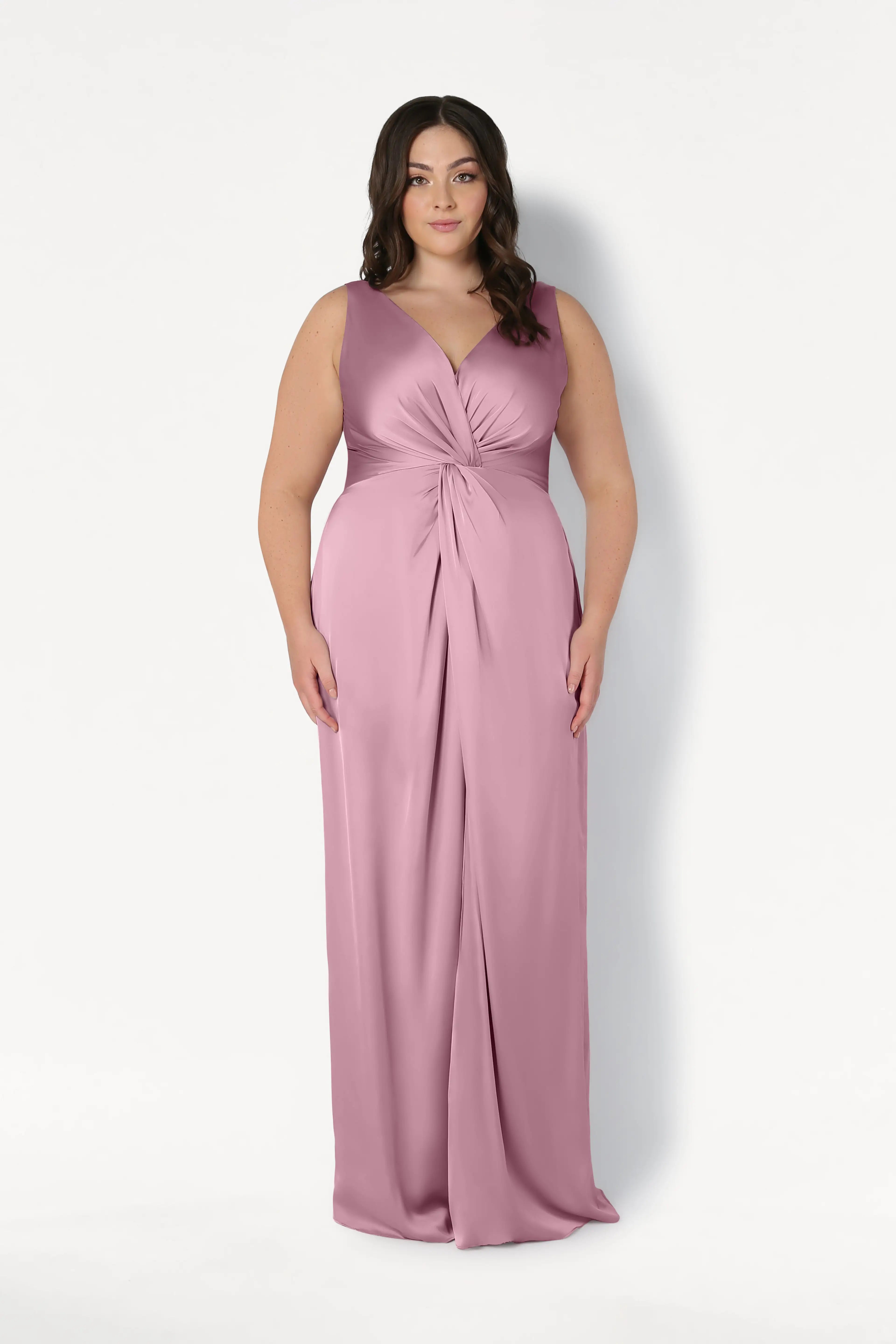 A woman models the TH&TH Carmen Bridesmaid Dress in rose pink satin—a sleeveless, floor-length gown with a twist-knot waist and V-neckline—her loose waves completing this modern bridal party look.