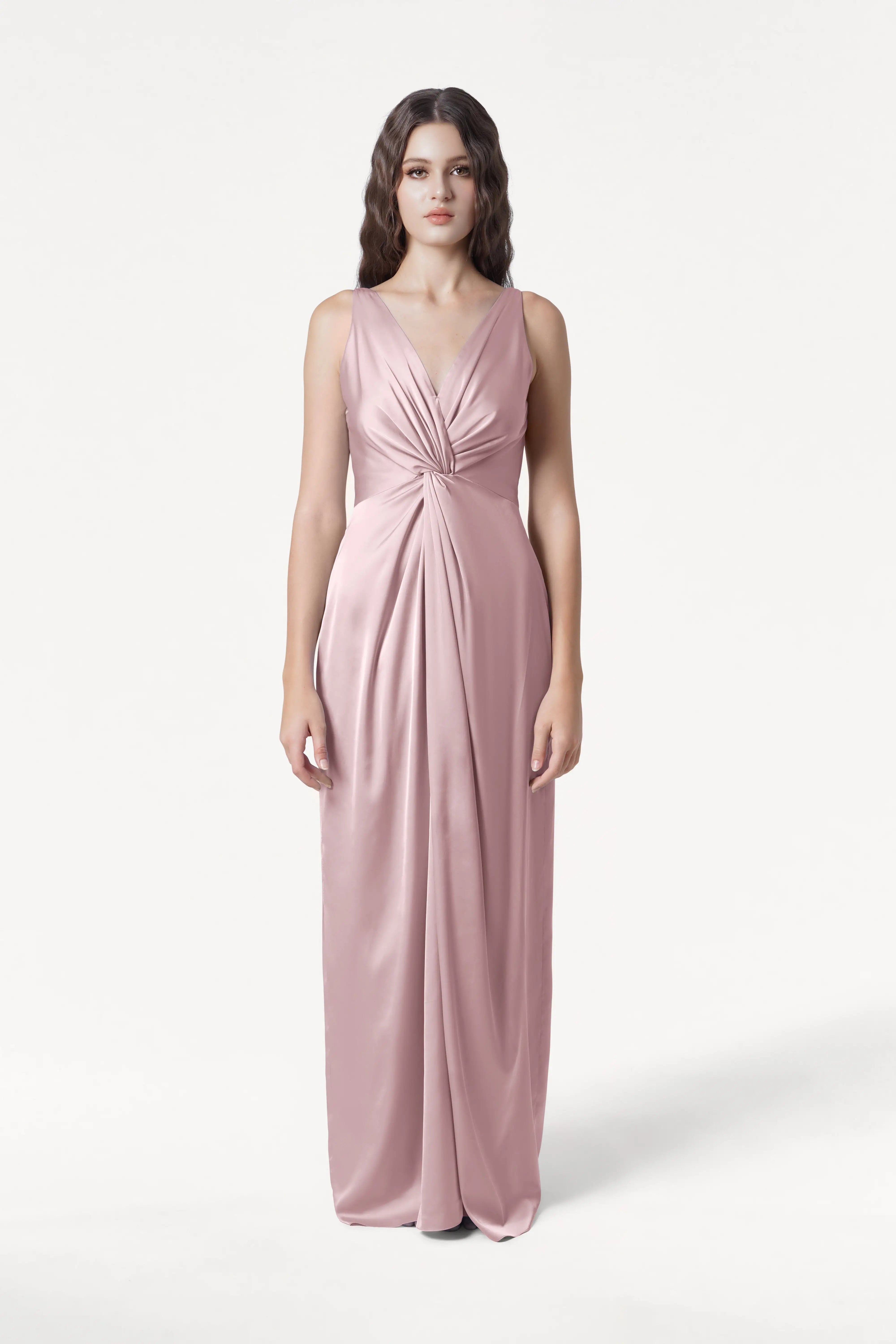 A woman poses against a white background in the TH&TH Carmen Bridesmaid Dress—an elegant, sleeveless, floor-length smoked blush satin gown with a deep V-neckline and gathered waist, ideal for modern bridal parties.