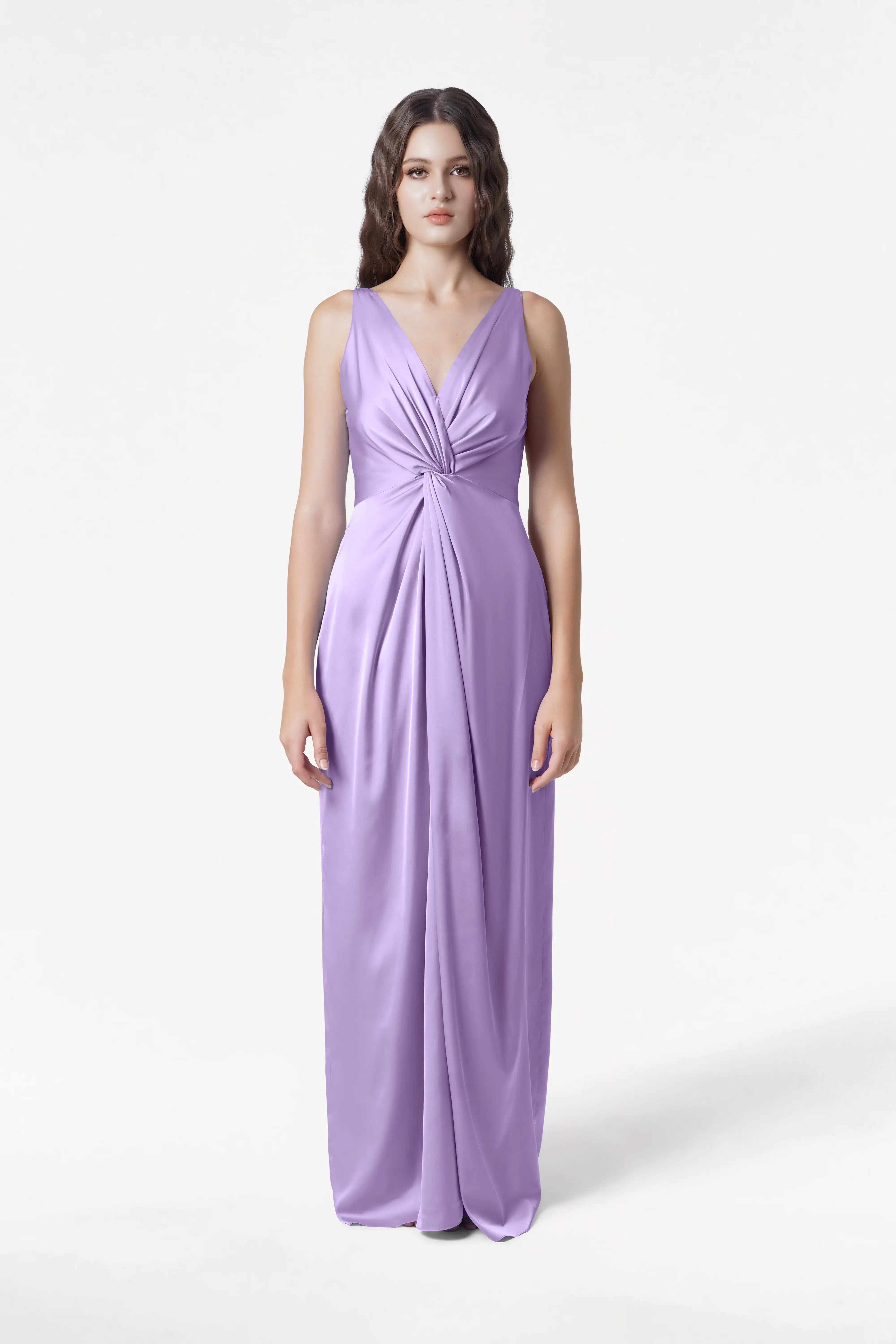 A woman stands facing forward in the TH&TH Carmen Bridesmaid Dress in Violet Satin—a floor-length, sleeveless gown with a deep V-neck and gathered pleats at the waist—set against a plain white background.