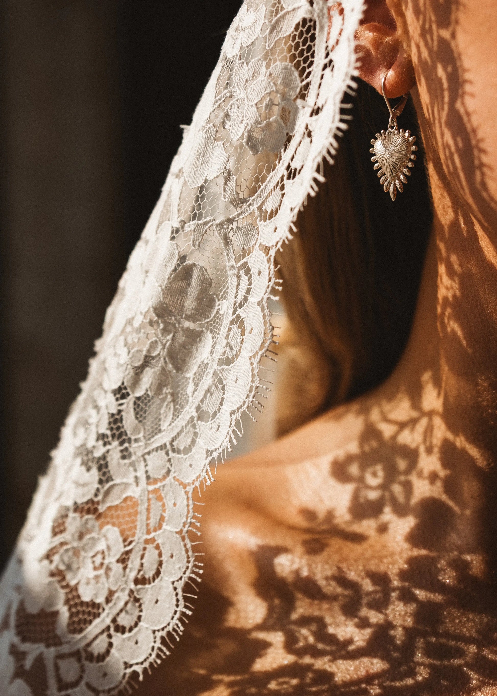 Close-up of a person wearing the Catherine Eyelash Lace Mantilla Veil by TH&TH, its delicate lace casting intricate shadows on their skin, with a heart-shaped earring visible.