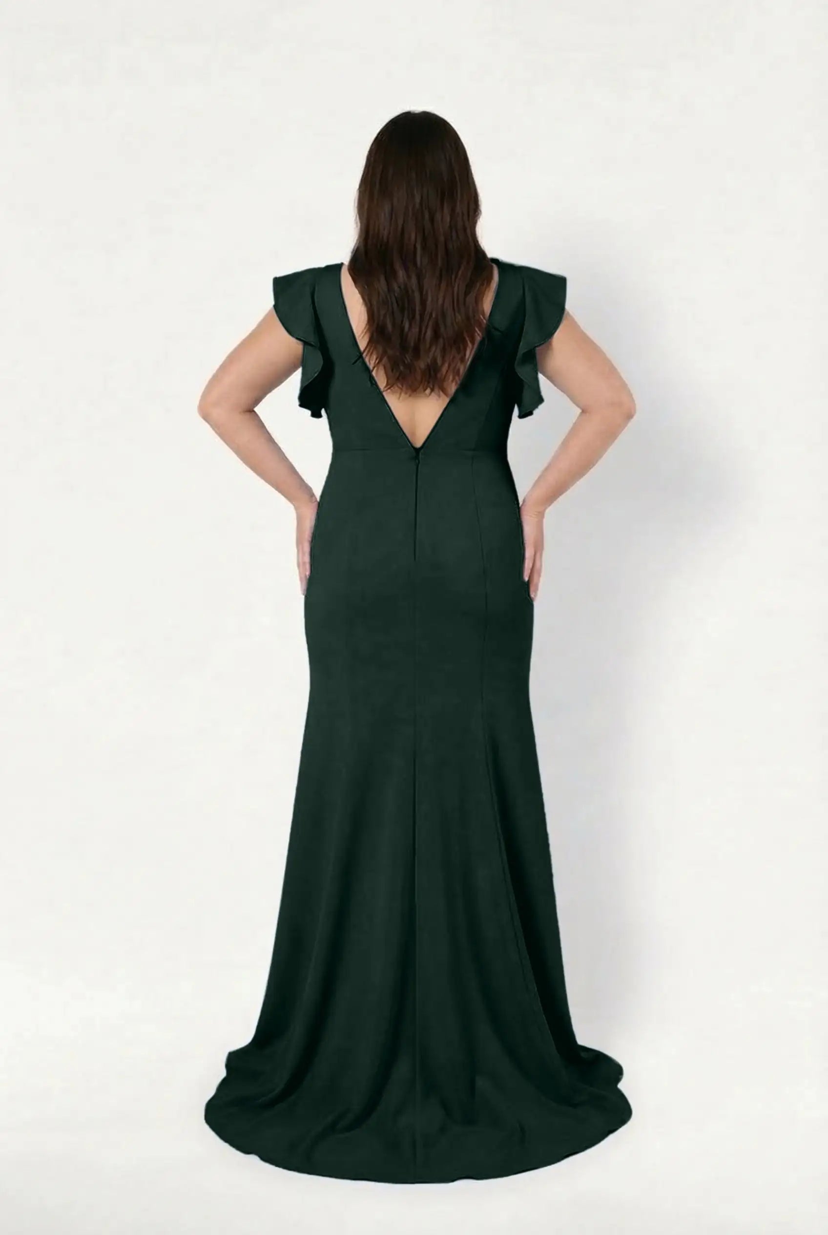 A woman with long brown hair faces away, modeling the TH&TH Cecelia Moss Crepe Bridesmaid Dress in Forest Green, featuring ruffled short sleeves and a deep V-back, against a plain white background.