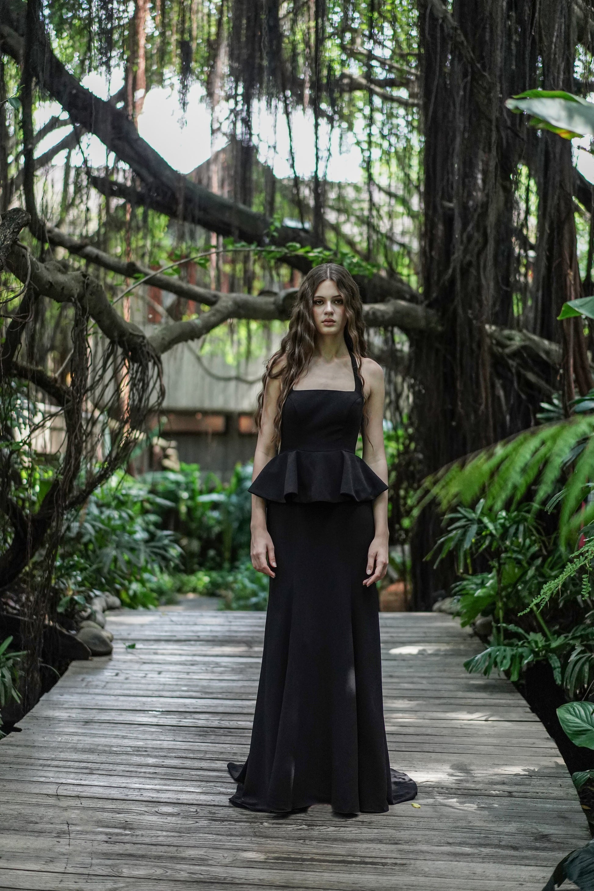 Woman wearing black peplum gown in a forest setting.