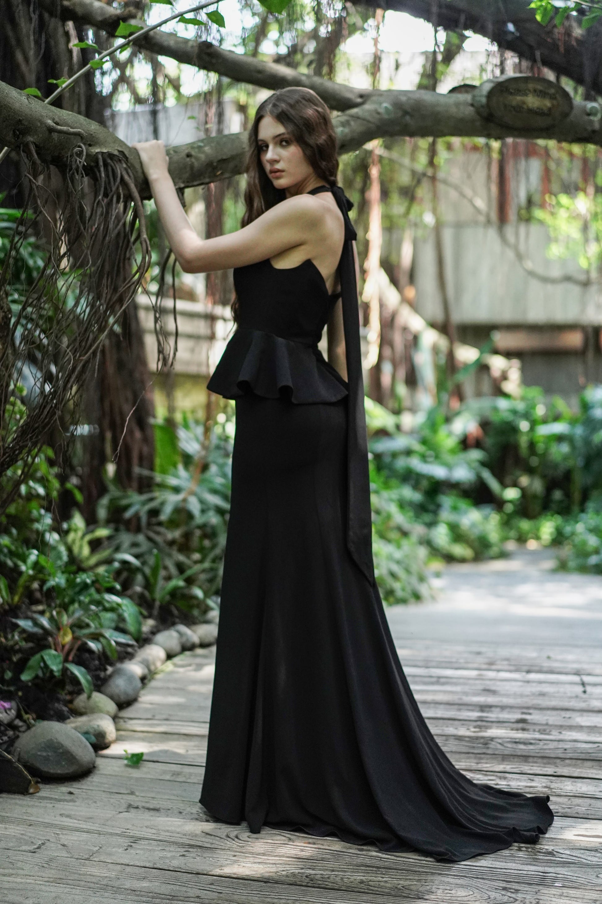 Woman wearing black peplum dress side view with train on skirt.