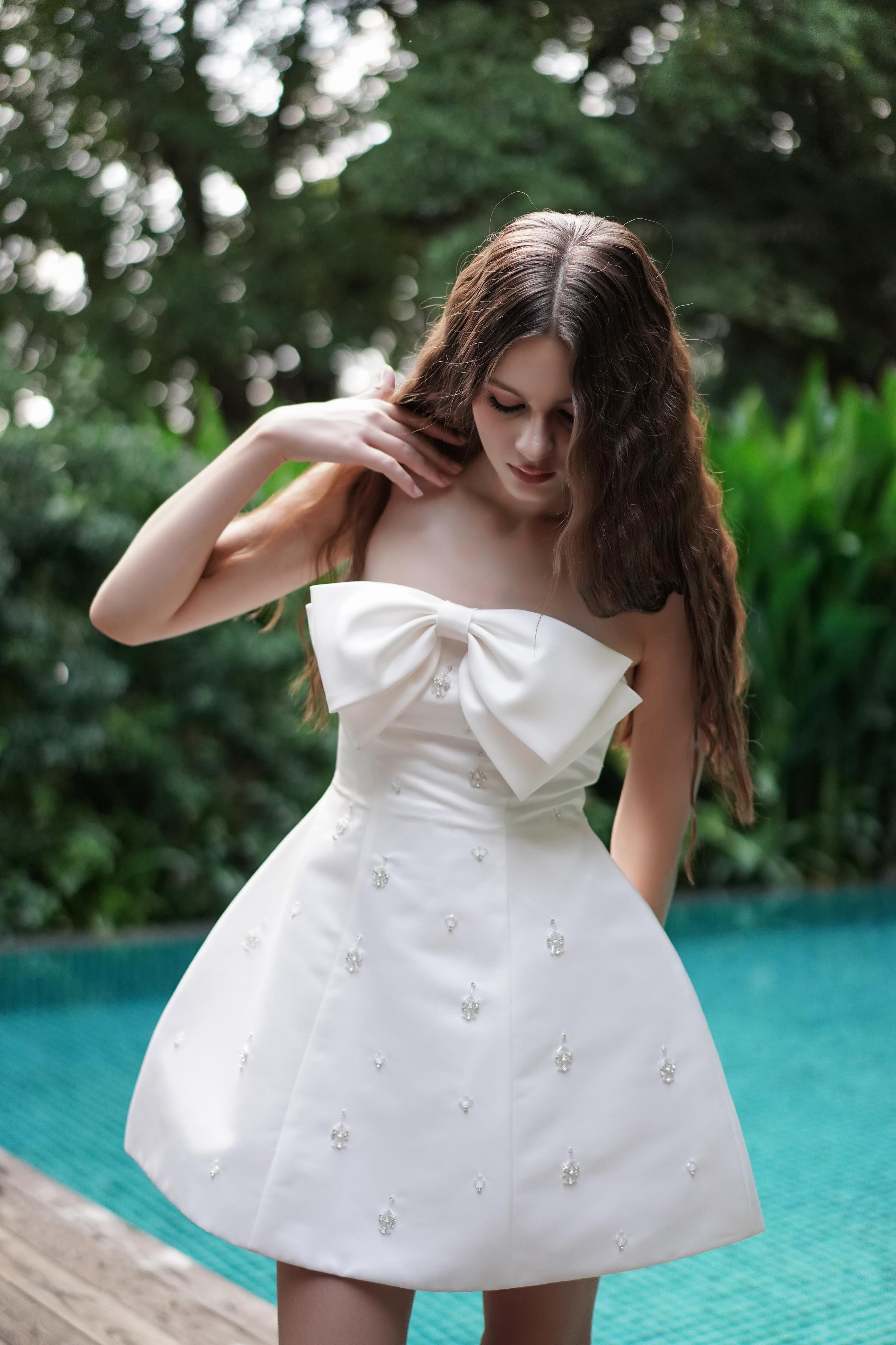 Woman in a white dress standing by a pool with greenery in the background