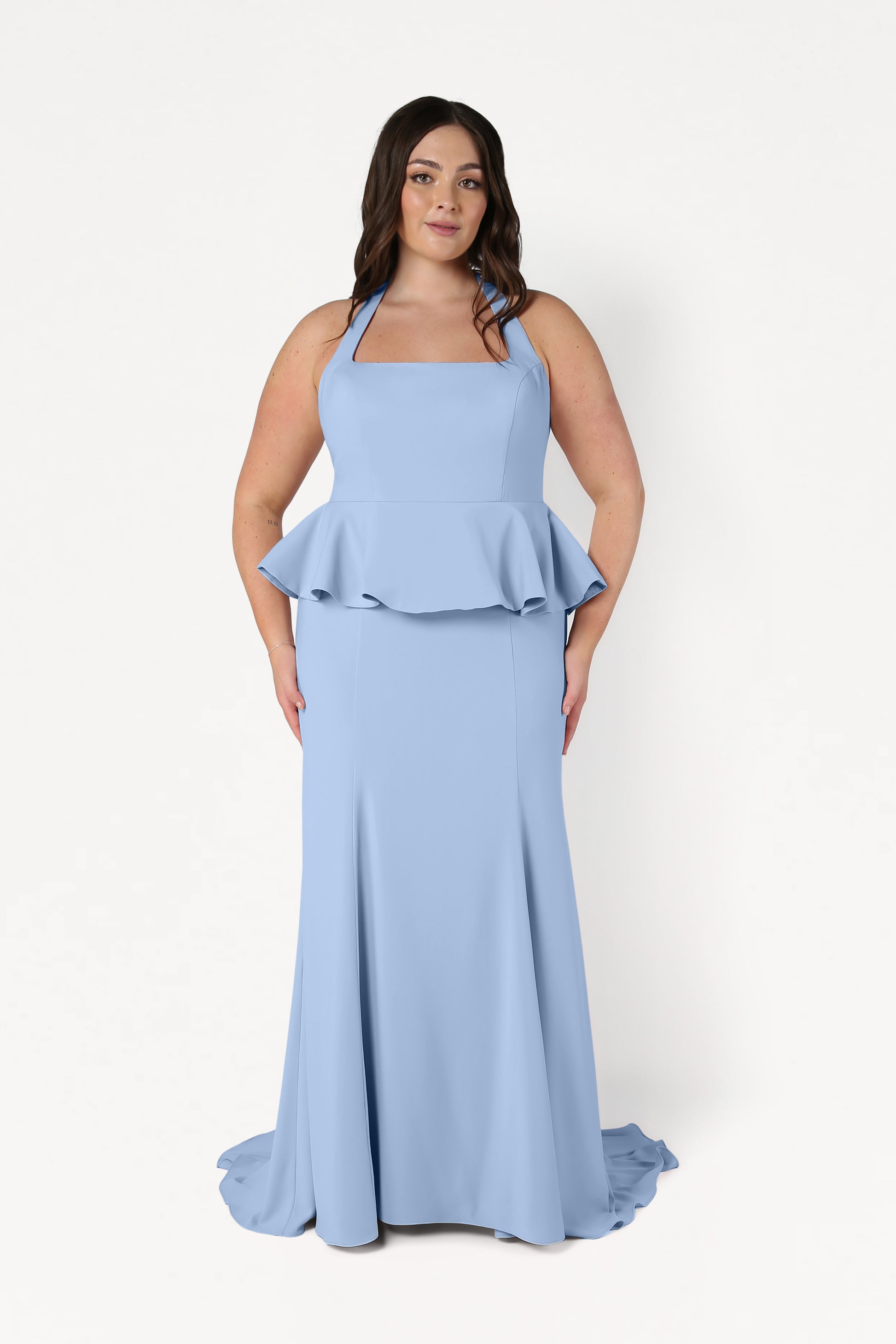 A woman wearing the TH&TH Peony Bridesmaid Dress in Dusty Blue, featuring a sleeveless, floor-length design with a square neckline and peplum waist, stands against a white background.