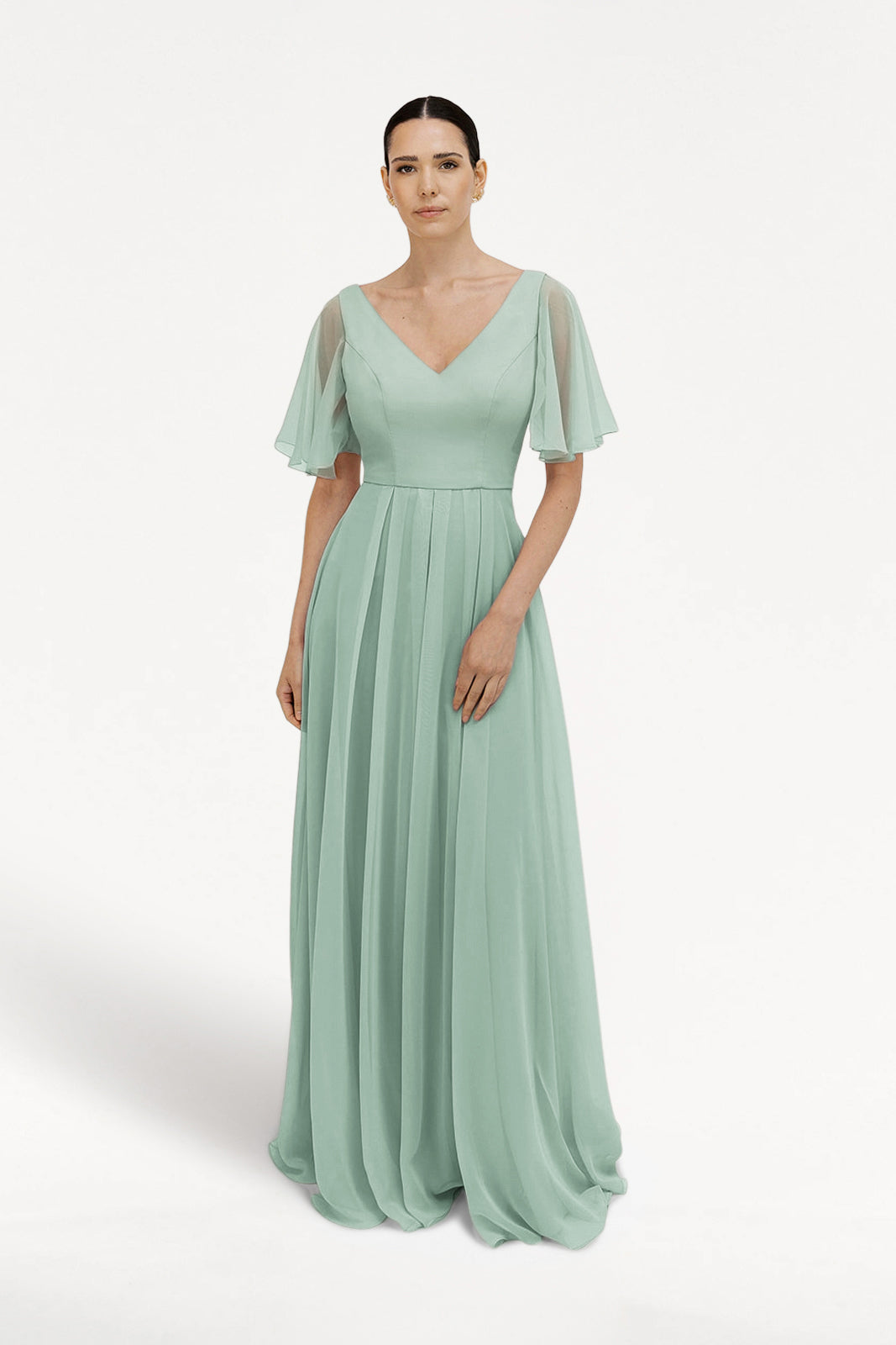 A woman with dark hair pulled back models the TH&TH Phoebe Bridesmaid Dress in Dusty Eucalyptus chiffon, a floor-length gown featuring a V-neckline, sheer flutter sleeves, and a pleated skirt against a white background.