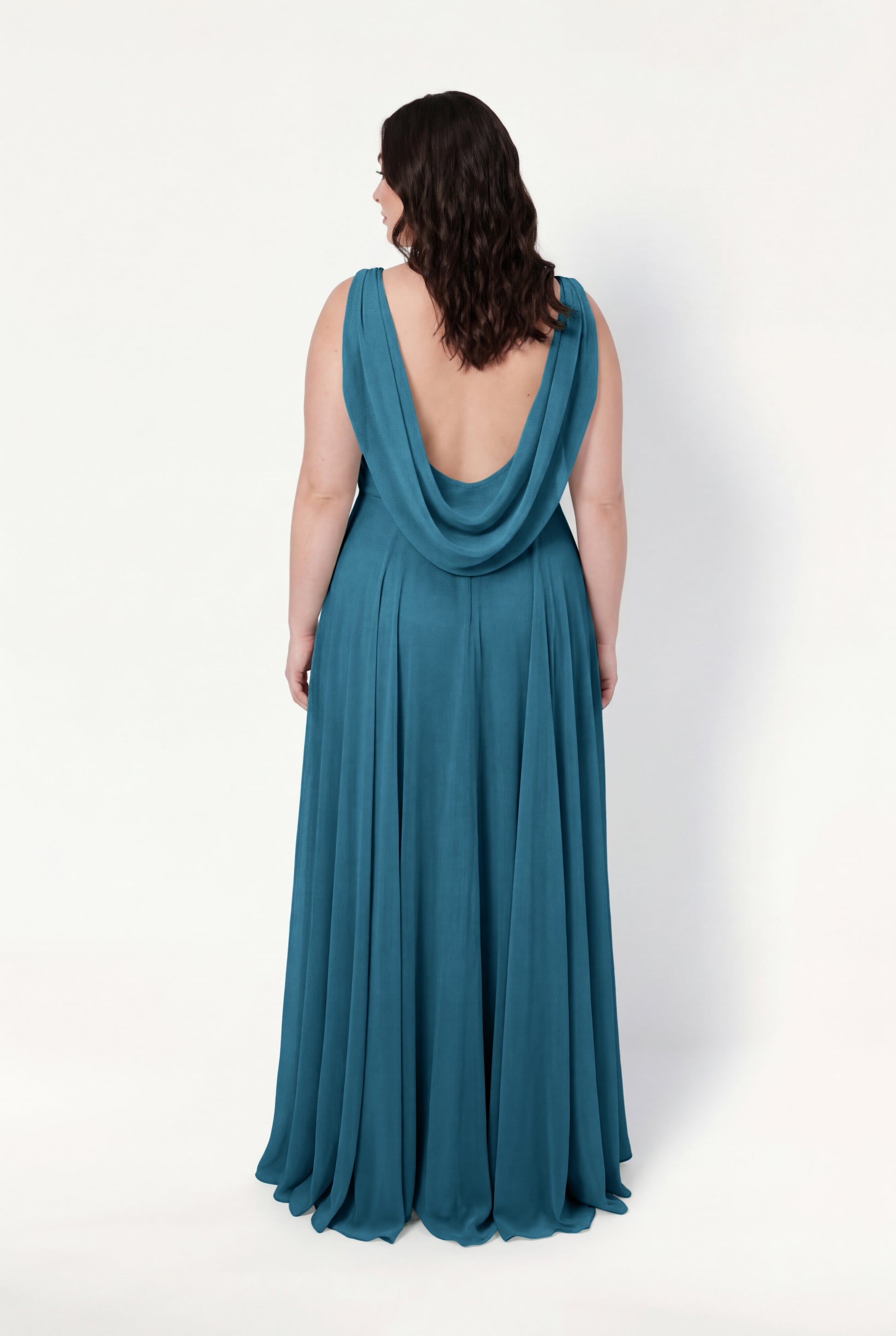 A woman stands with her back to the camera against a white background, wearing the TH&TH Athena Bridesmaid Dress in Emerald Dawn—a sleeveless, floor-length chiffon gown with a draped low-cut back, exuding timeless elegance.