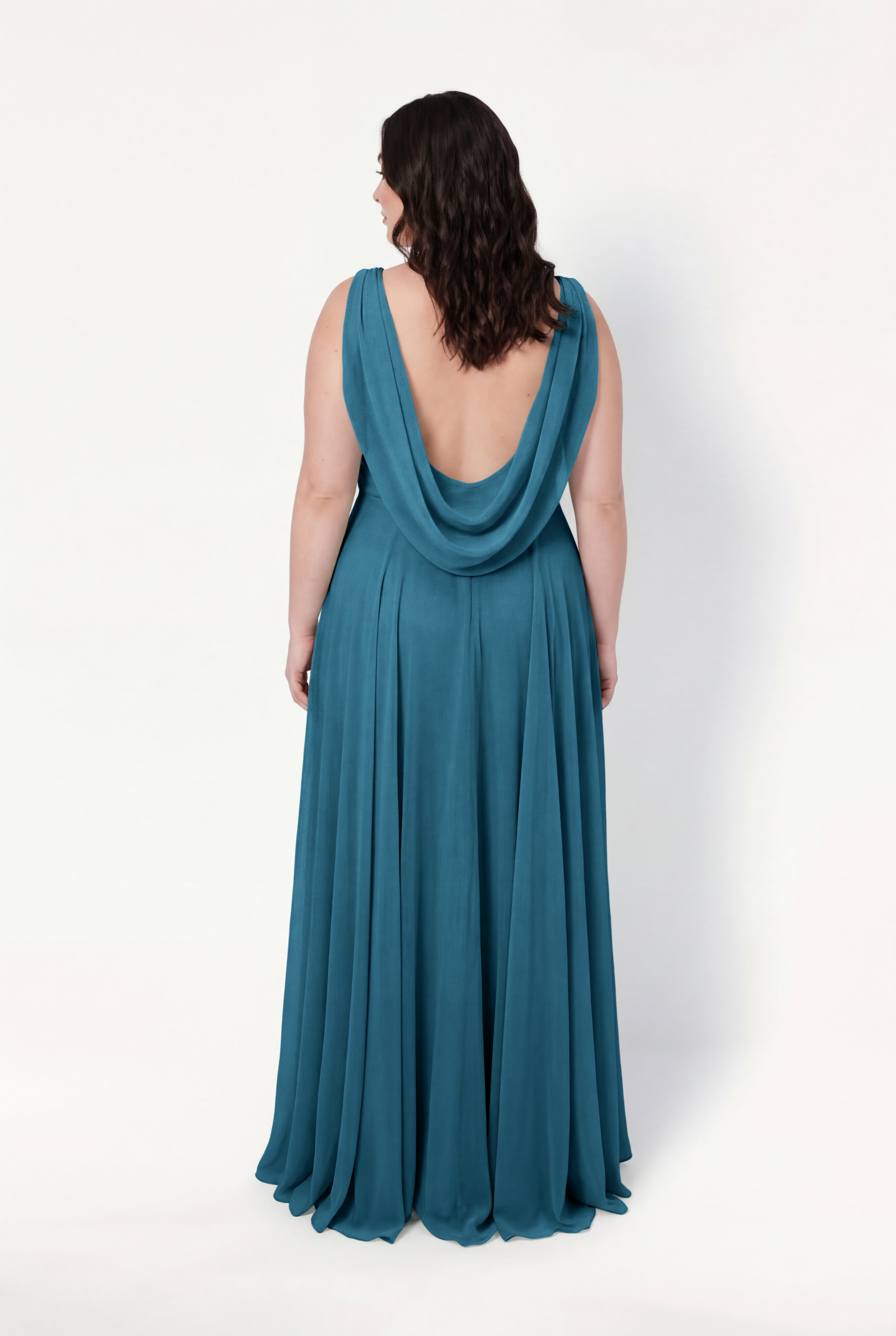 A woman stands with her back to the camera against a white background, wearing the TH&TH Athena Bridesmaid Dress in Emerald Dawn—a sleeveless, floor-length chiffon gown with a draped low-cut back, exuding timeless elegance.
