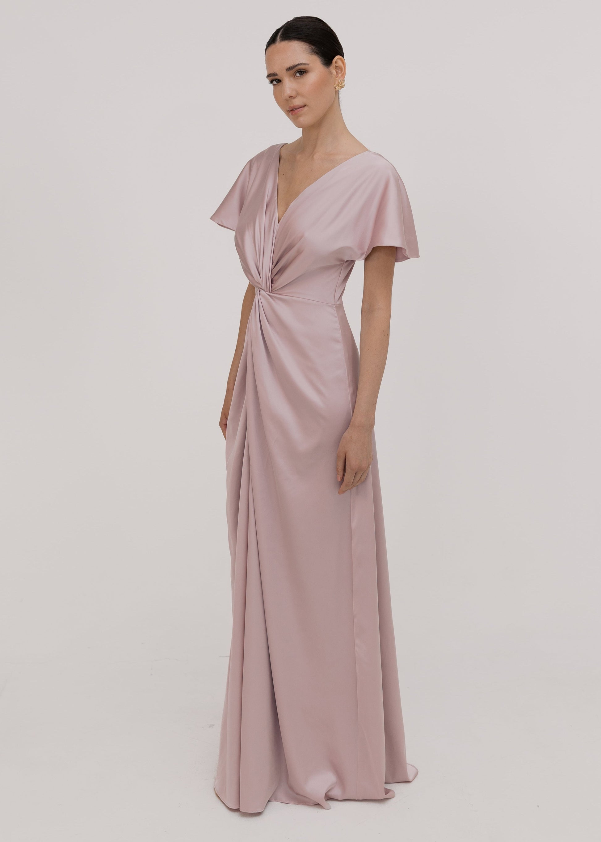Woman wearing a long smoked blush pink bridesmaid dress with sleeves, bra friendly high back and twist knot detail in satin.