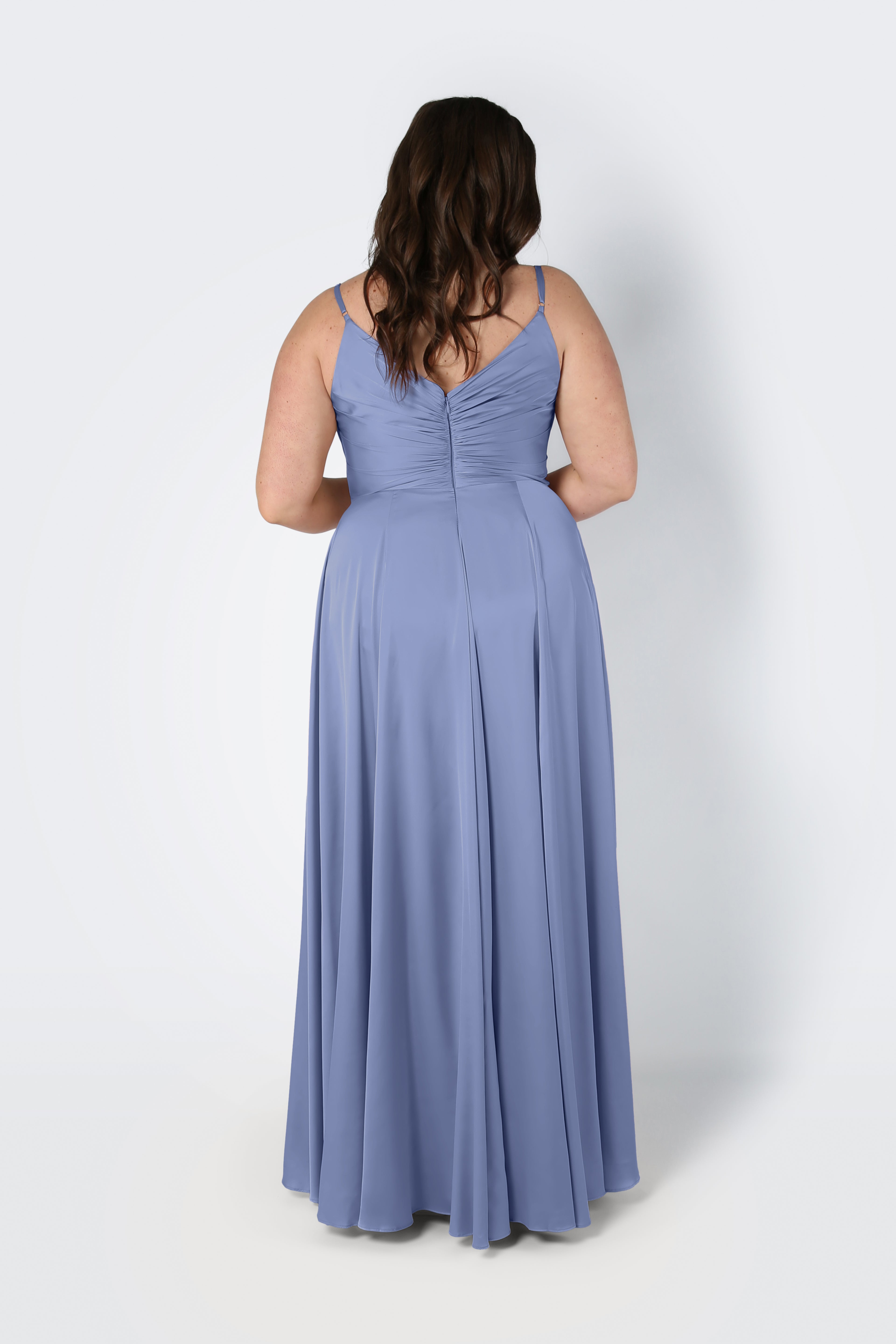 Back view of a woman wearing the TH&TH Isla Bridesmaid Dress in French Blue Satin, featuring spaghetti straps, a pleated bodice with ruched back, and a flowing floor-length A-line skirt.