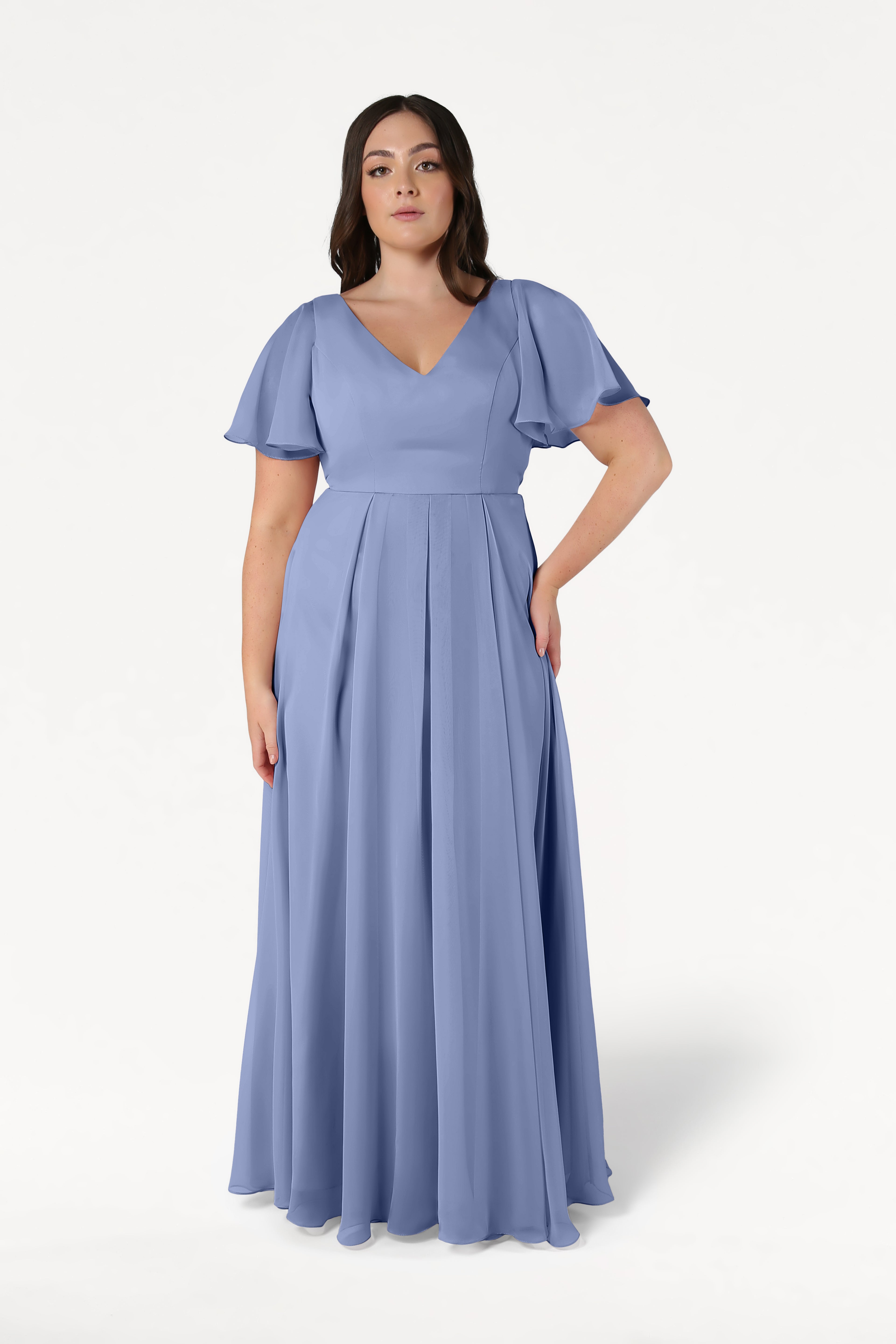 A woman wears the TH&TH Phoebe Bridesmaid Dress in French Blue Chiffon, a floor-length gown with short flutter sleeves and a V-neckline, standing against a plain white background.