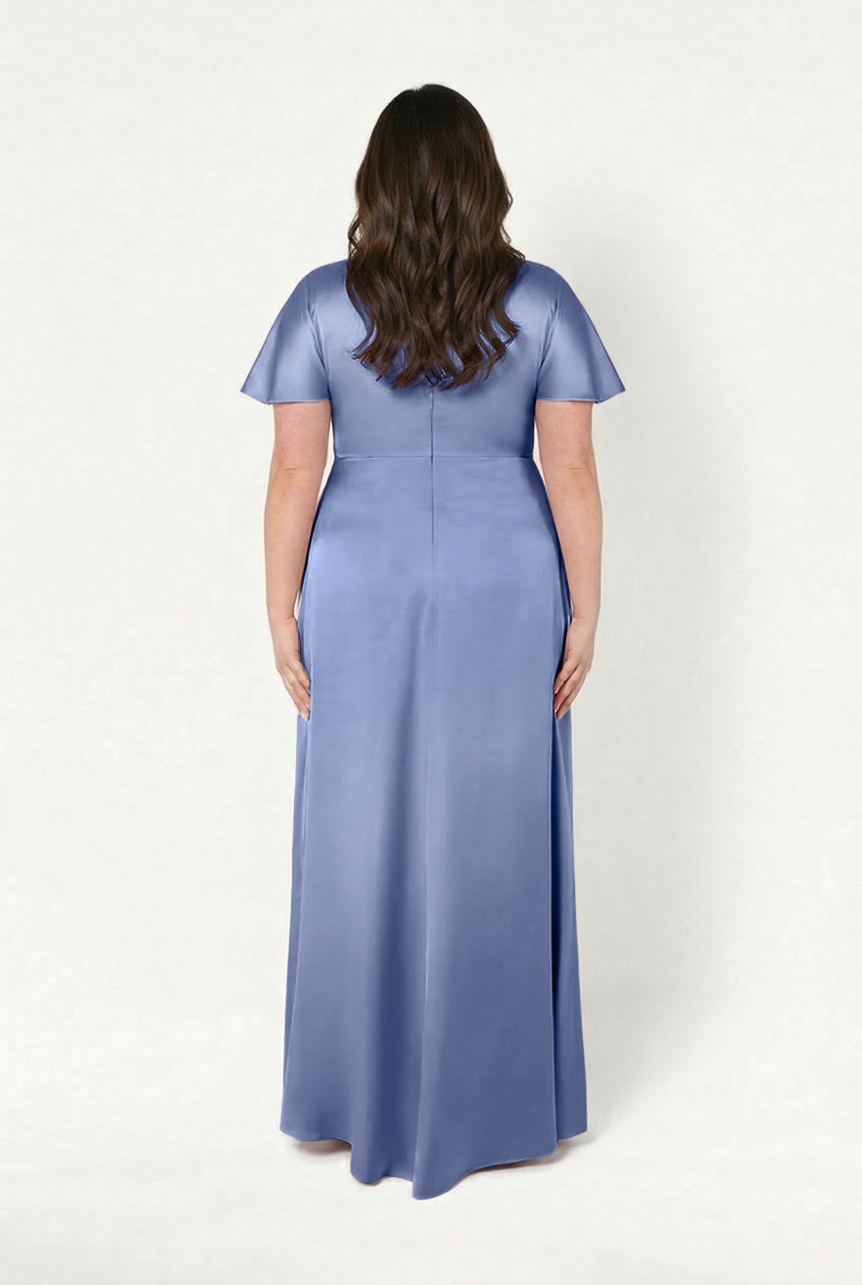 A woman with wavy brown hair is seen from behind wearing the TH&TH Camilla Bridesmaid Dress in French Blue Satin, a size-inclusive, floor-length gown with short sleeves, set against a plain light background.