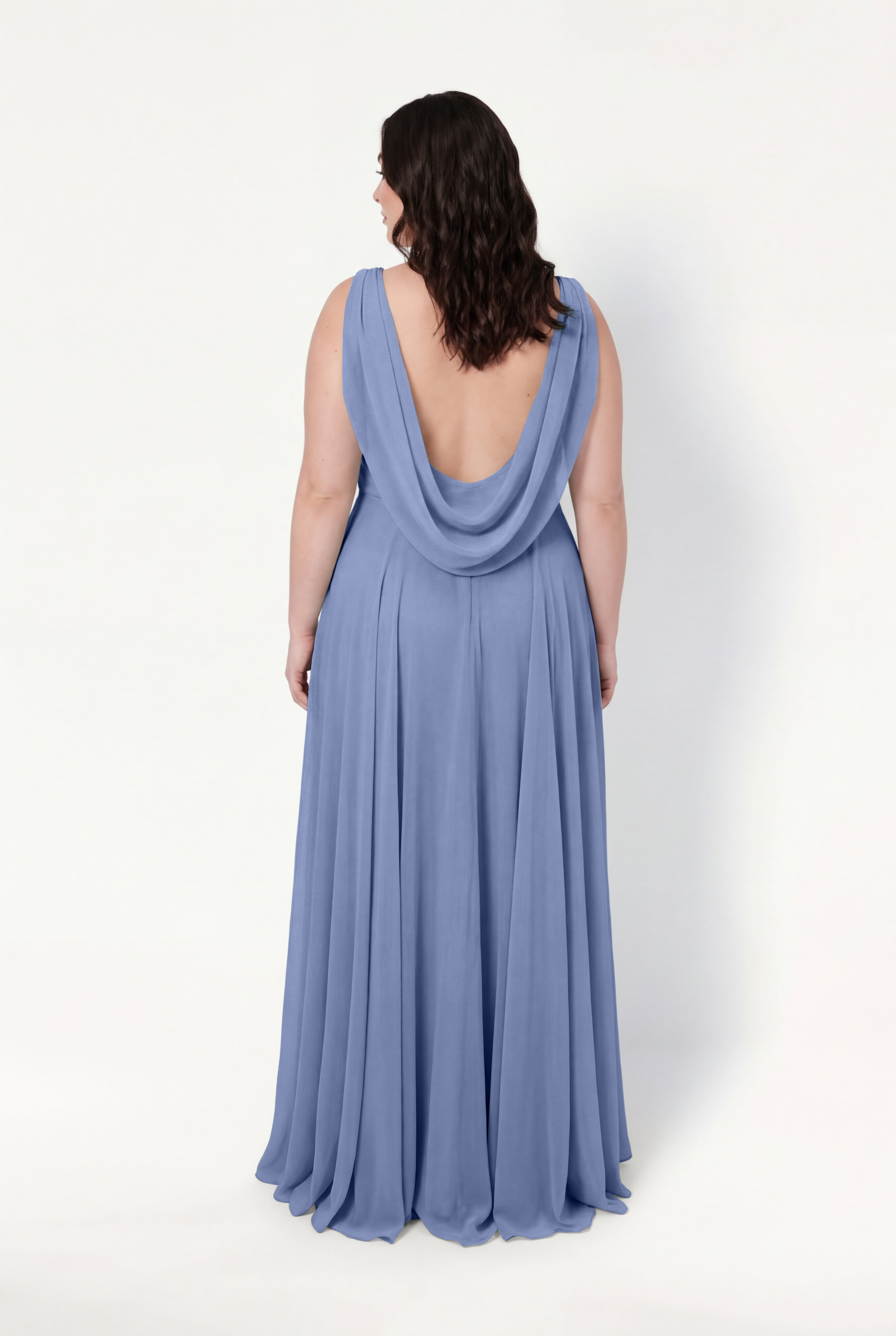 A woman with wavy brown hair faces away, showcasing the TH&TH Athena Bridesmaid Dress in French Blue Chiffon. The sleeveless gown features a draped cowl and open back, elegantly set against a plain white background.