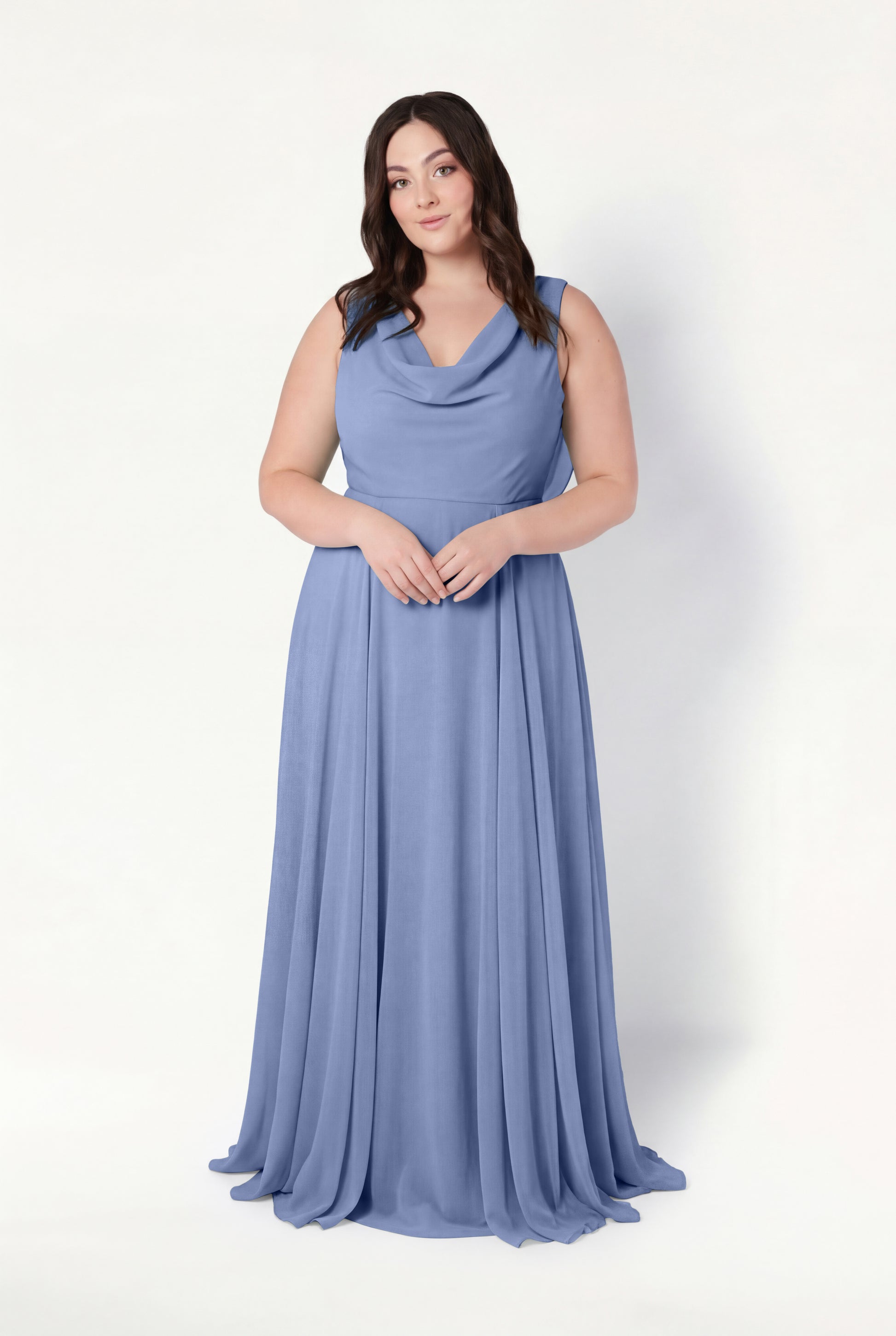 A woman with long brown hair wears the TH&TH Athena Bridesmaid Dress in French Blue Chiffon, featuring a sleeveless, floor-length design and cowl neck, standing against a plain white background with her hands clasped in front.