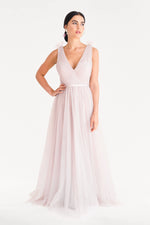 A woman wears the TH&TH Grace Bridesmaid Dress in Smoked Blush Tulle, featuring a deep V-neck and ribbon shoulder details, standing against a plain white background.