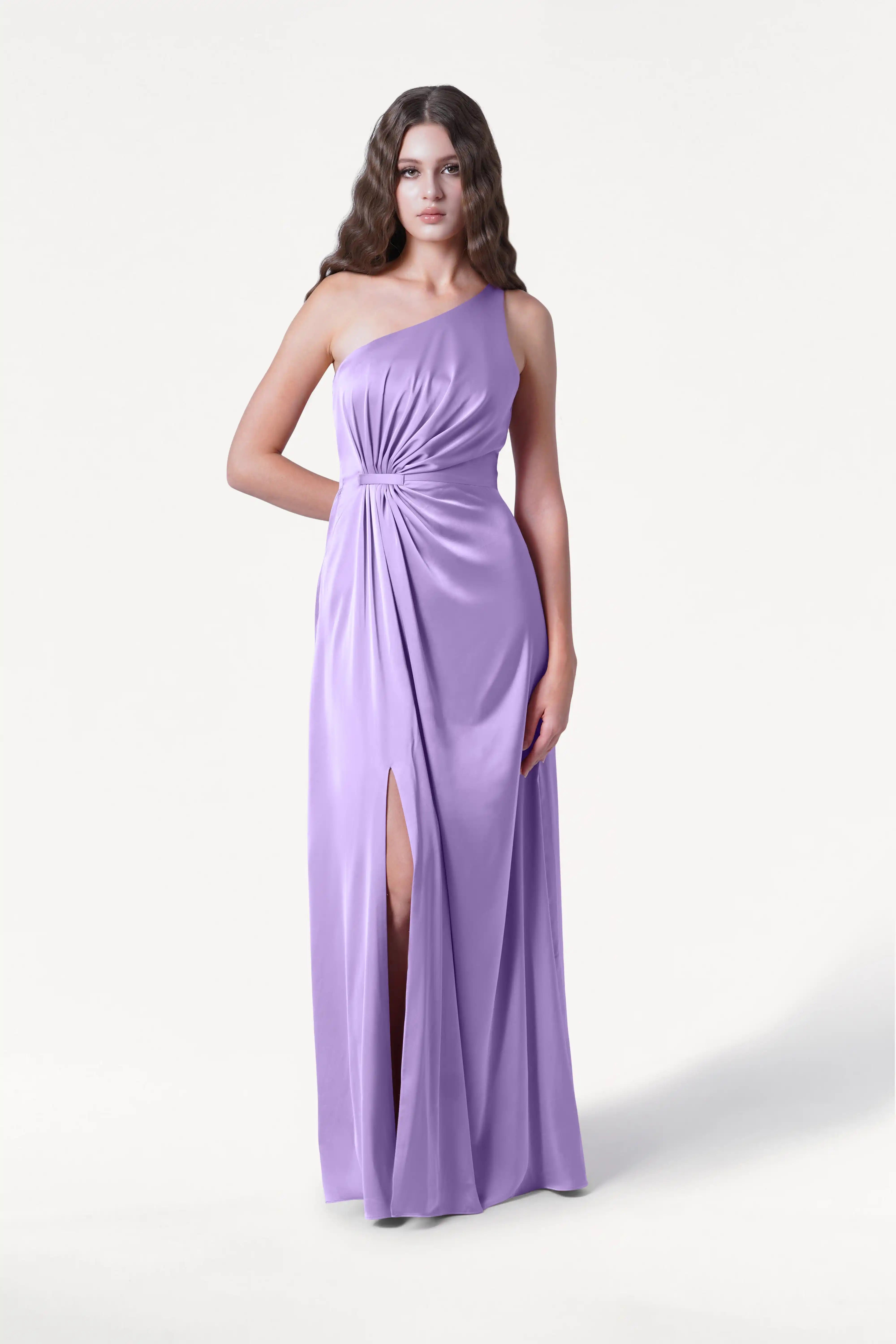 A woman models the TH&TH Greta Bridesmaid Dress in violet satin, a sleeveless one-shoulder gown with Grecian draping, a gathered waist, and a thigh-high slit, set against a plain white background.