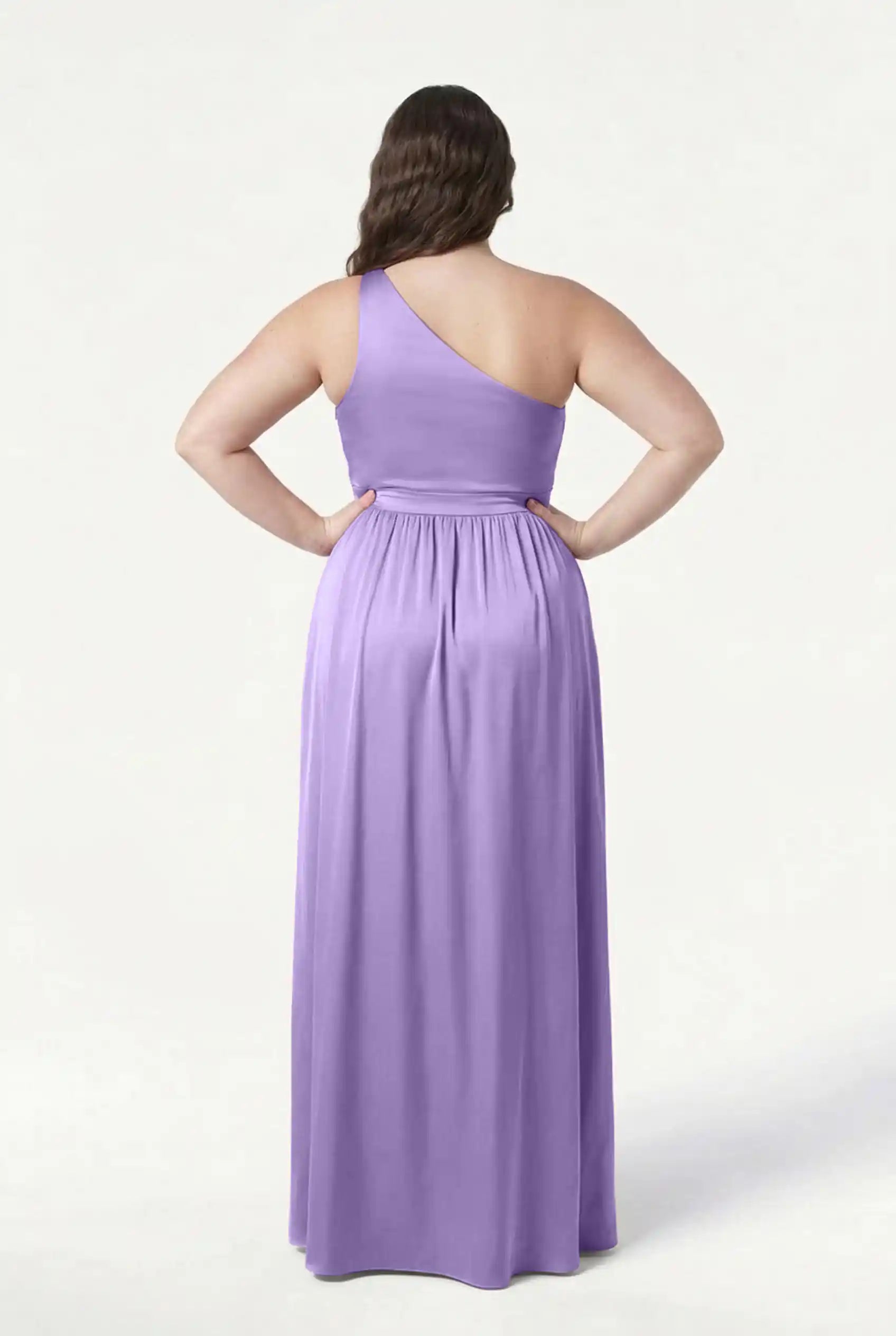 A woman stands with hands on hips, shown from the back against a plain white backdrop, wearing the TH&TH Greta Bridesmaid Dress in violet satin, featuring elegant Grecian-inspired draping.