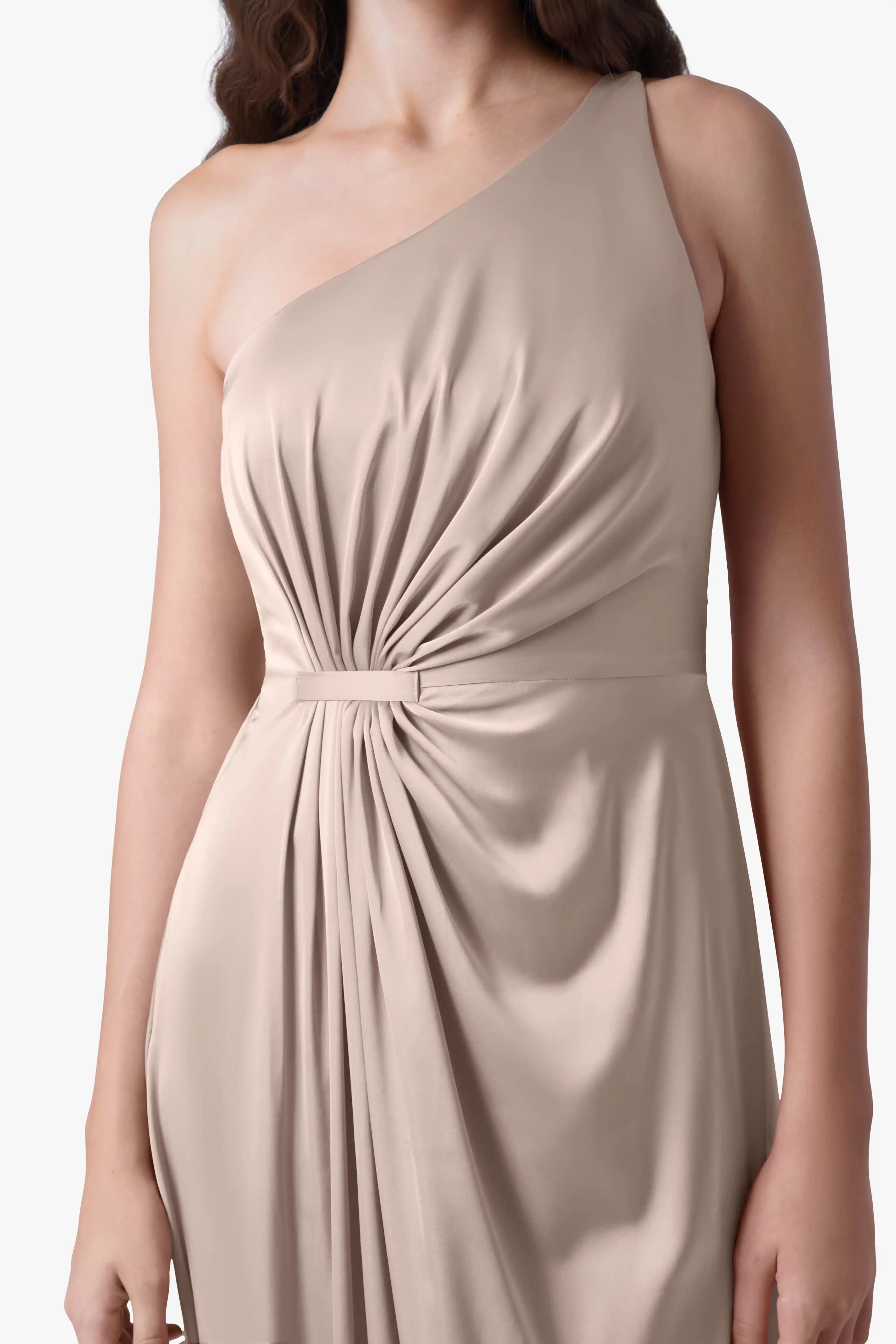 A woman models the TH&TH Greta Bridesmaid Dress in Champagne Sky Satin—sleeveless, one-shoulder, with ruched waist detail. Only her upper body is visible against a plain background.