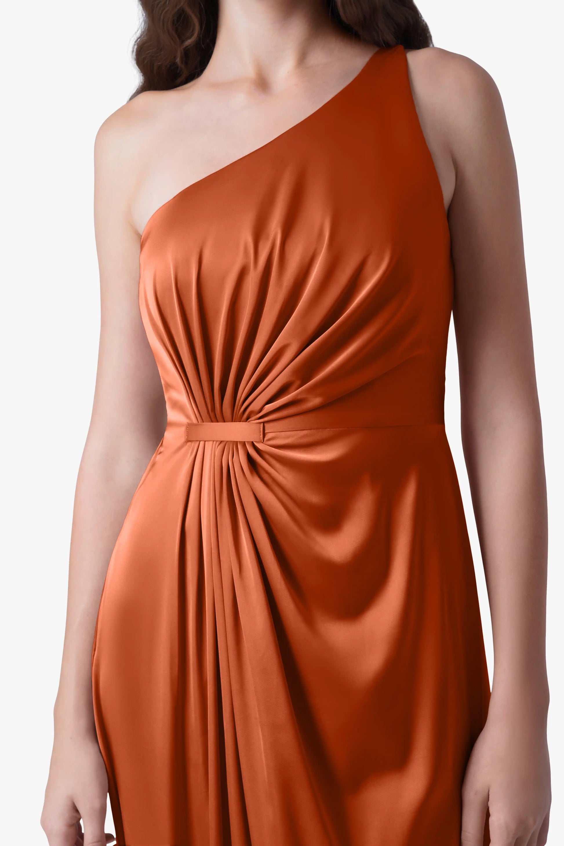 A woman models the TH&TH Greta Bridesmaid Dress in Terracotta Satin, featuring a sleeveless one-shoulder design with Grecian draping and gathered waist detail, standing against a plain background.