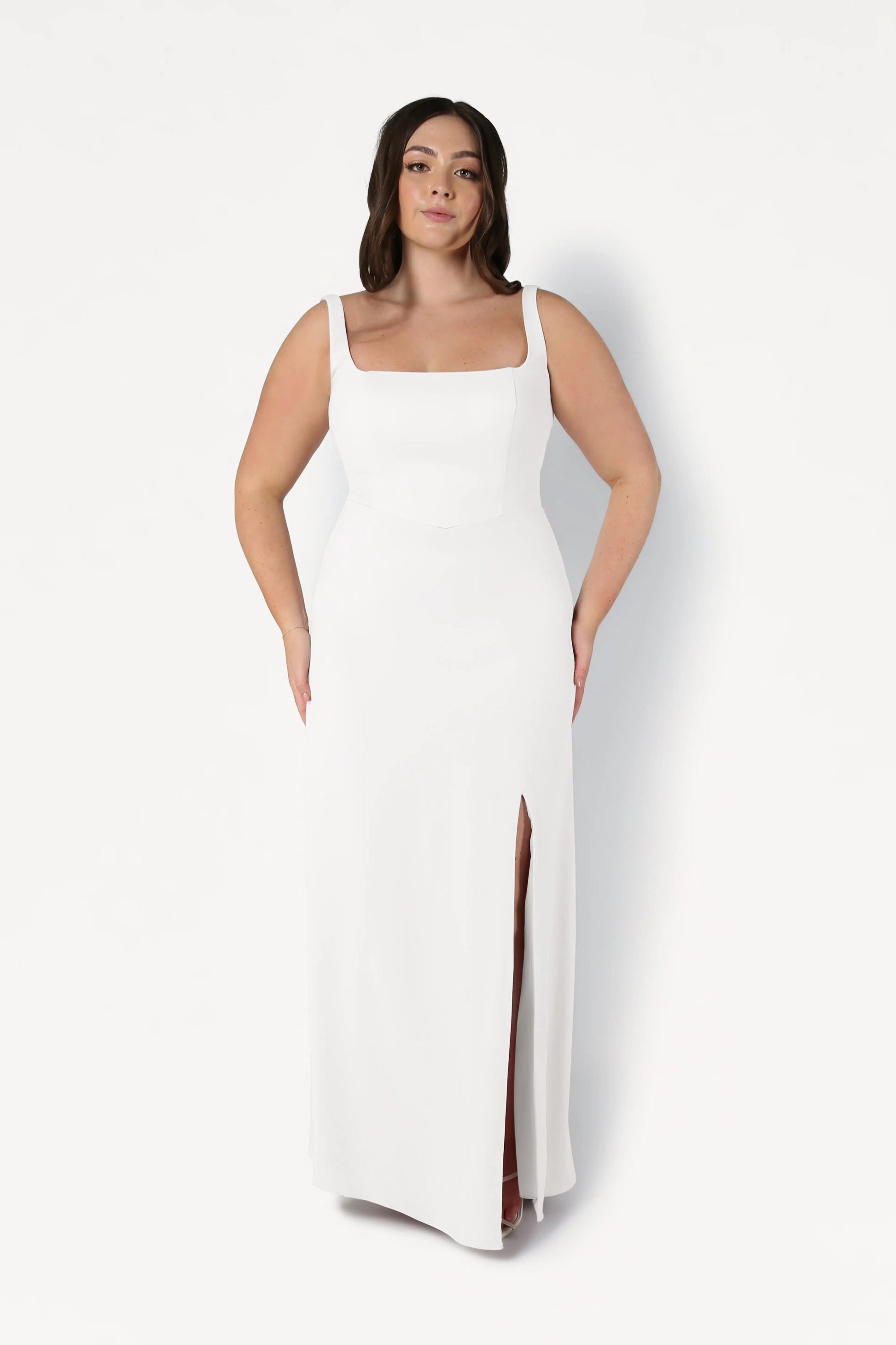 A woman stands against a plain white background wearing the TH&TH Helena Dress in Ivory, a sleeveless, floor-length moss crepe bridesmaid gown featuring a square neckline and thigh-high slit.