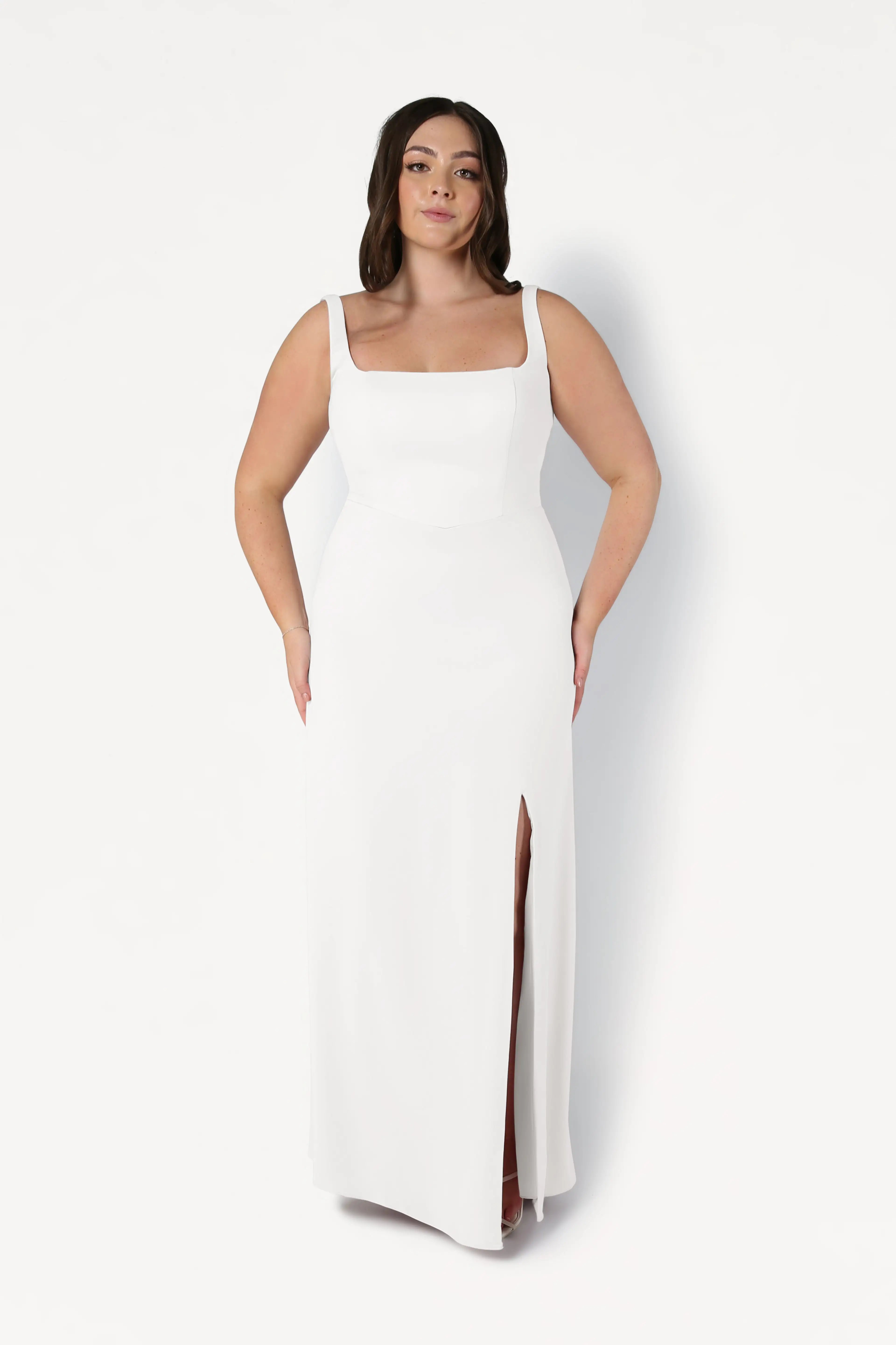 A woman stands against a plain white background wearing the TH&TH Helena Dress in Ivory, a sleeveless, floor-length moss crepe bridesmaid gown featuring a square neckline and thigh-high slit.