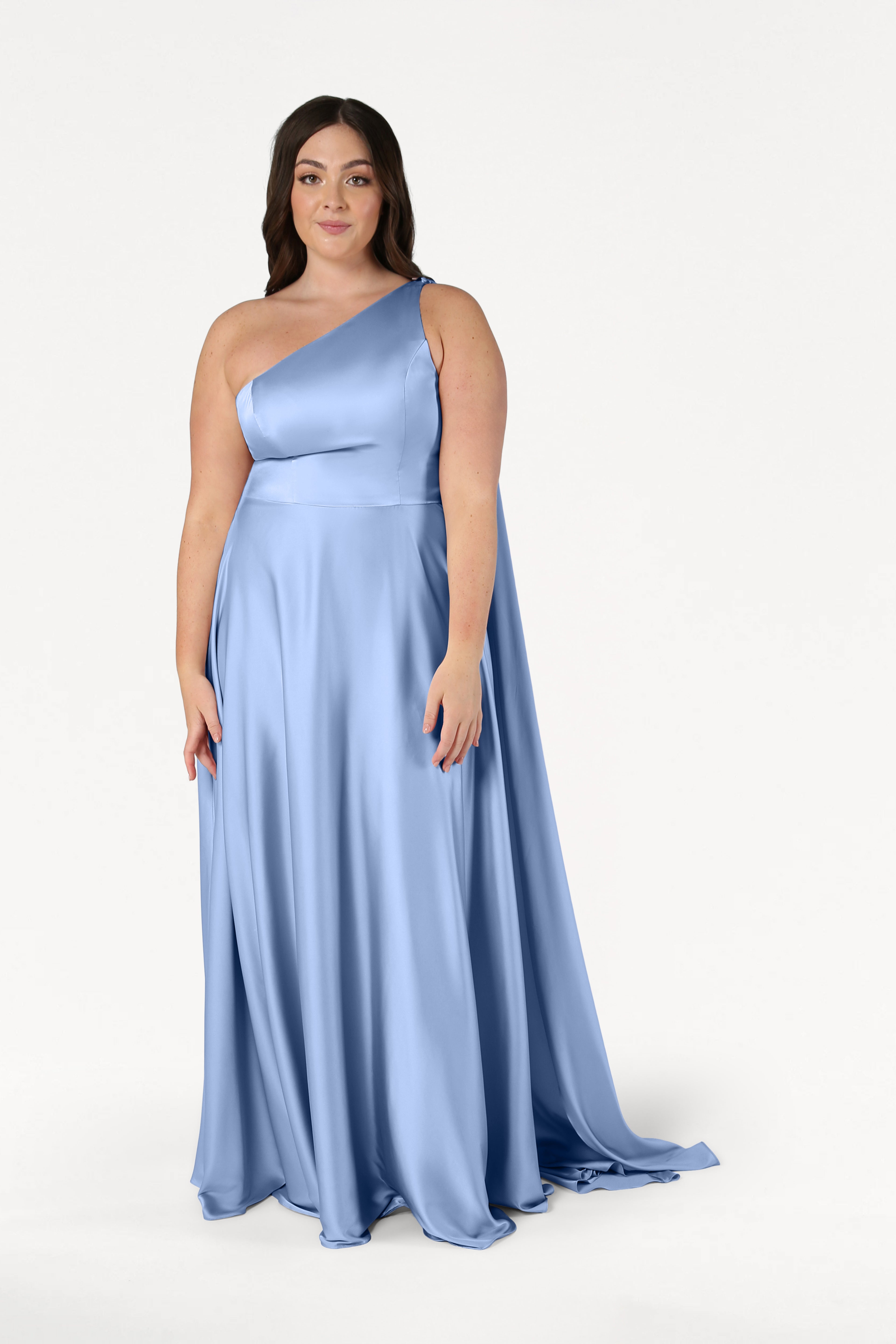 A woman stands facing forward against a plain white background, wearing the TH&TH Lyra Bridesmaid Dress in dusty blue satin.