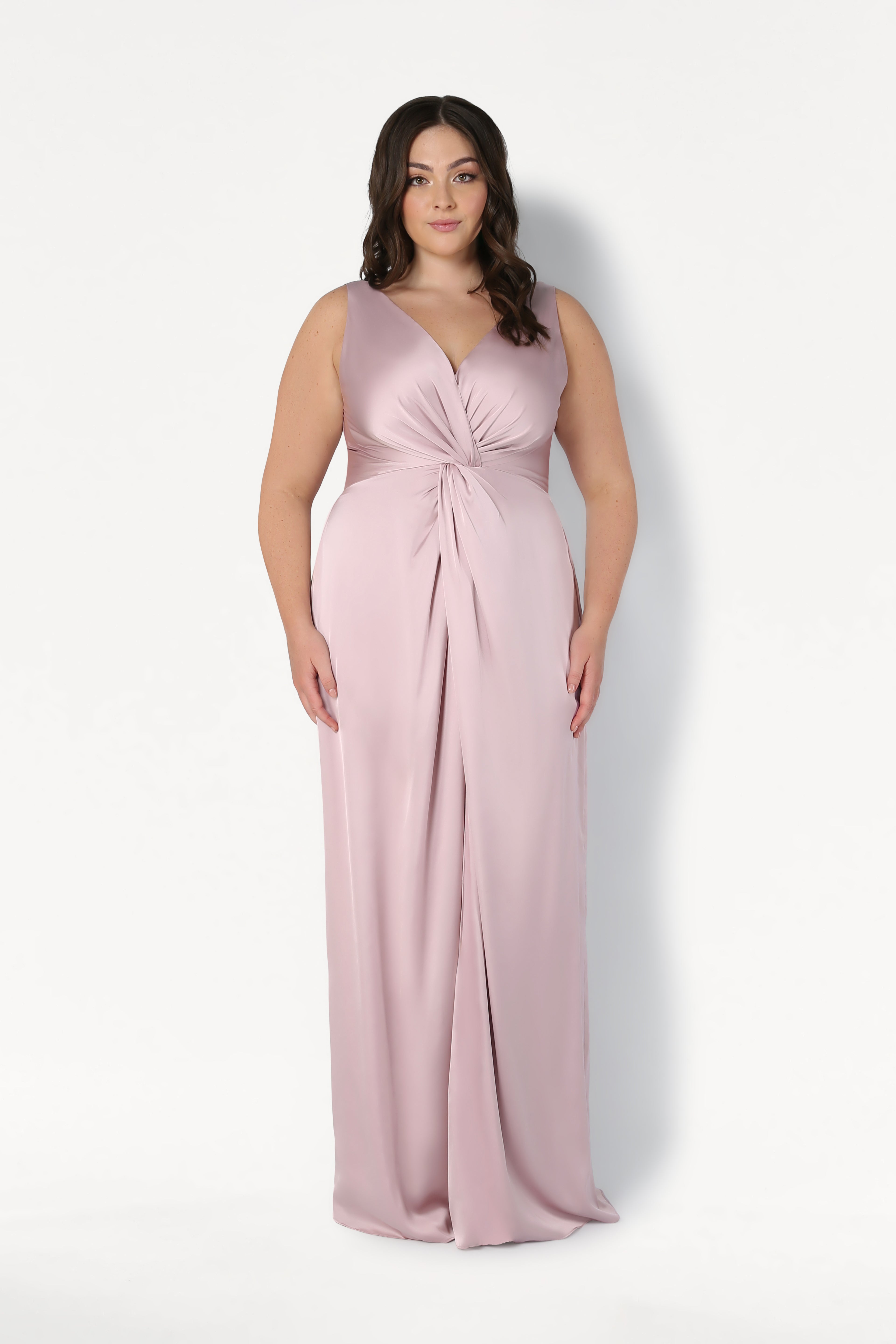 A woman models the TH&TH Carmen Bridesmaid Dress in smoked blush satin—a sleeveless, floor-length gown with a twisted knot waist detail—set against a plain white background, ideal for contemporary bridal parties.