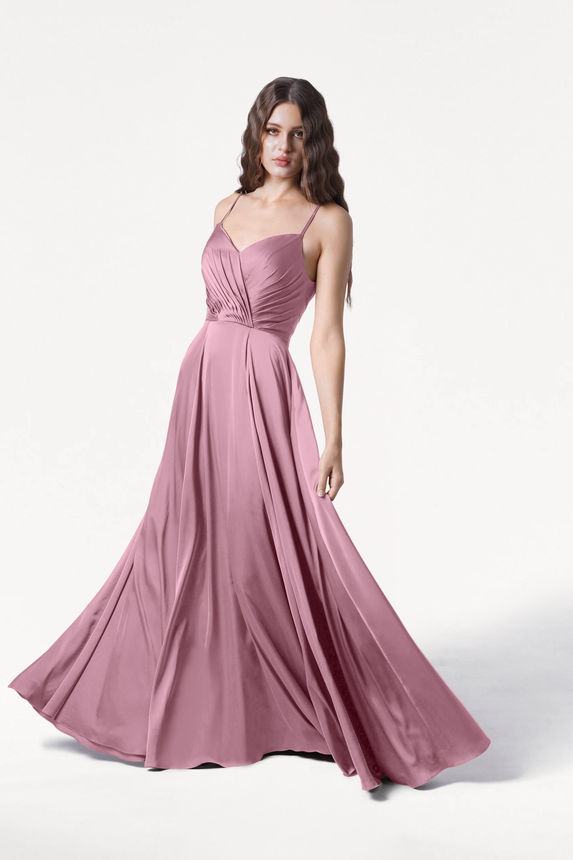 A woman stands against a plain white background wearing the TH&TH Isla Bridesmaid Dress in rose pink satin, featuring a flowing, floor-length silhouette, adjustable straps, and a fitted ruched bodice.
