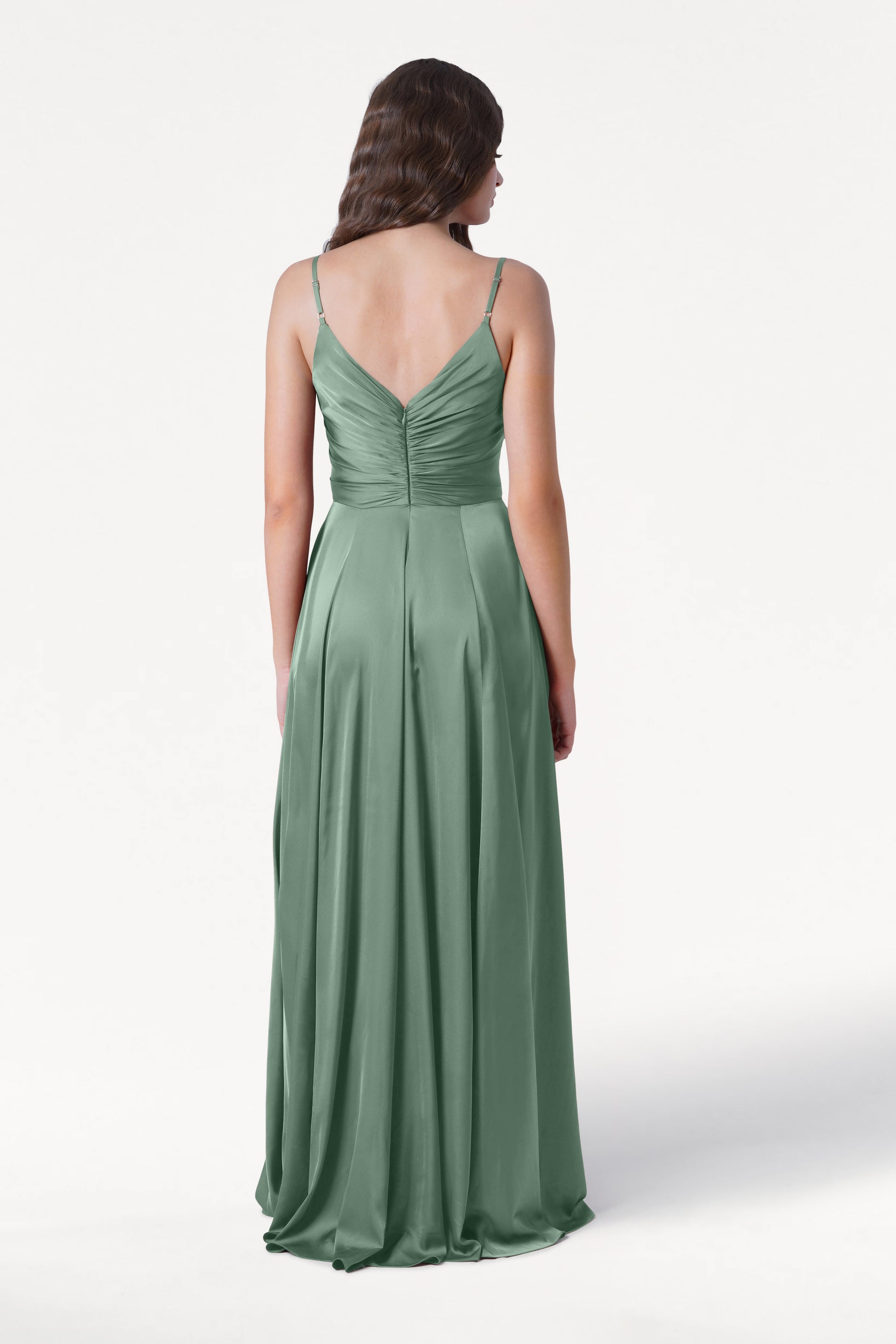 A woman wearing the TH&TH Isla Bridesmaid Dress in Sage Green Satin, featuring a pleated bodice, spaghetti straps, and a ruched back, stands against a plain white background, shown from behind.