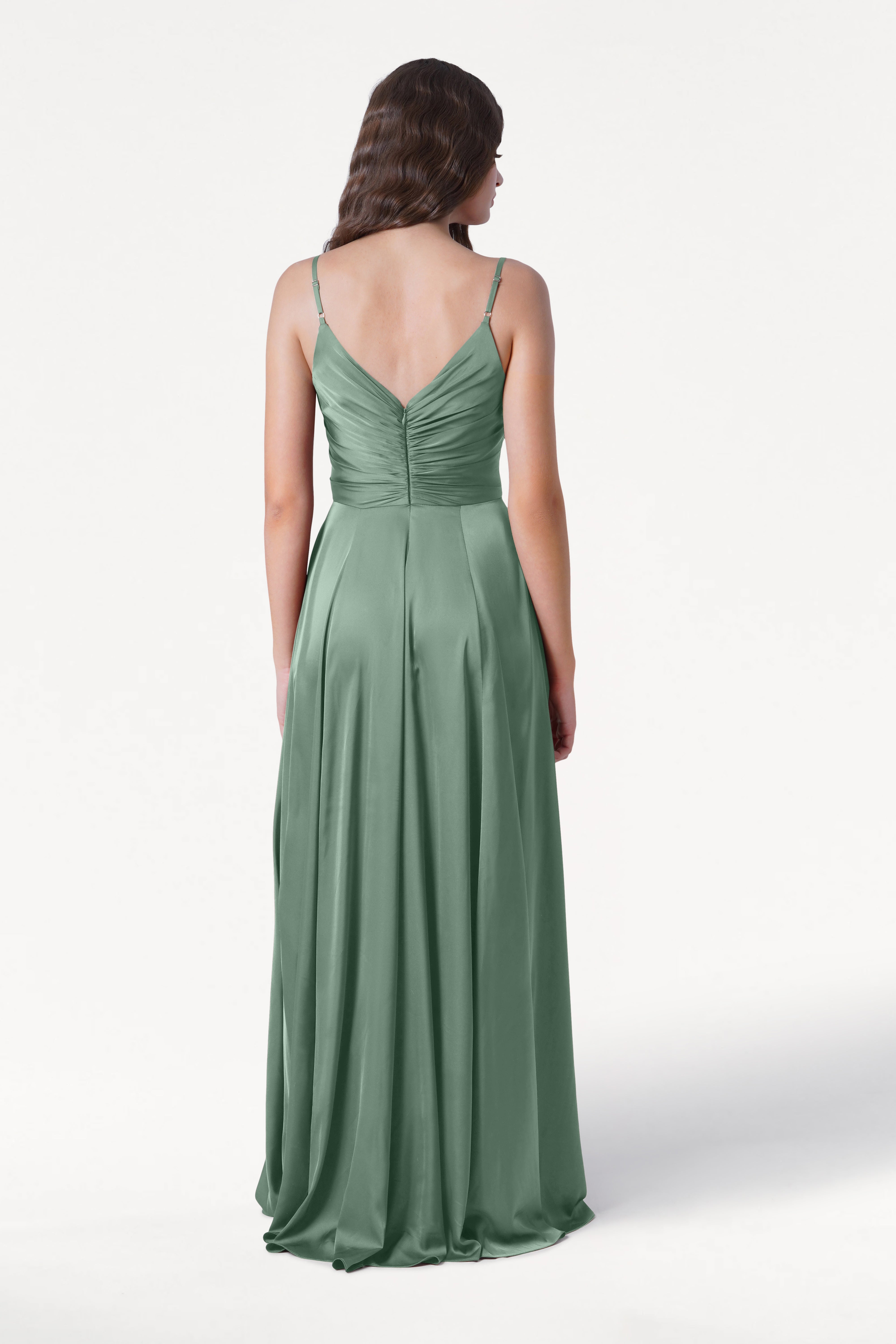 A woman wearing the TH&TH Isla Bridesmaid Dress in Sage Green Satin, featuring a pleated bodice, spaghetti straps, and a ruched back, stands against a plain white background, shown from behind.