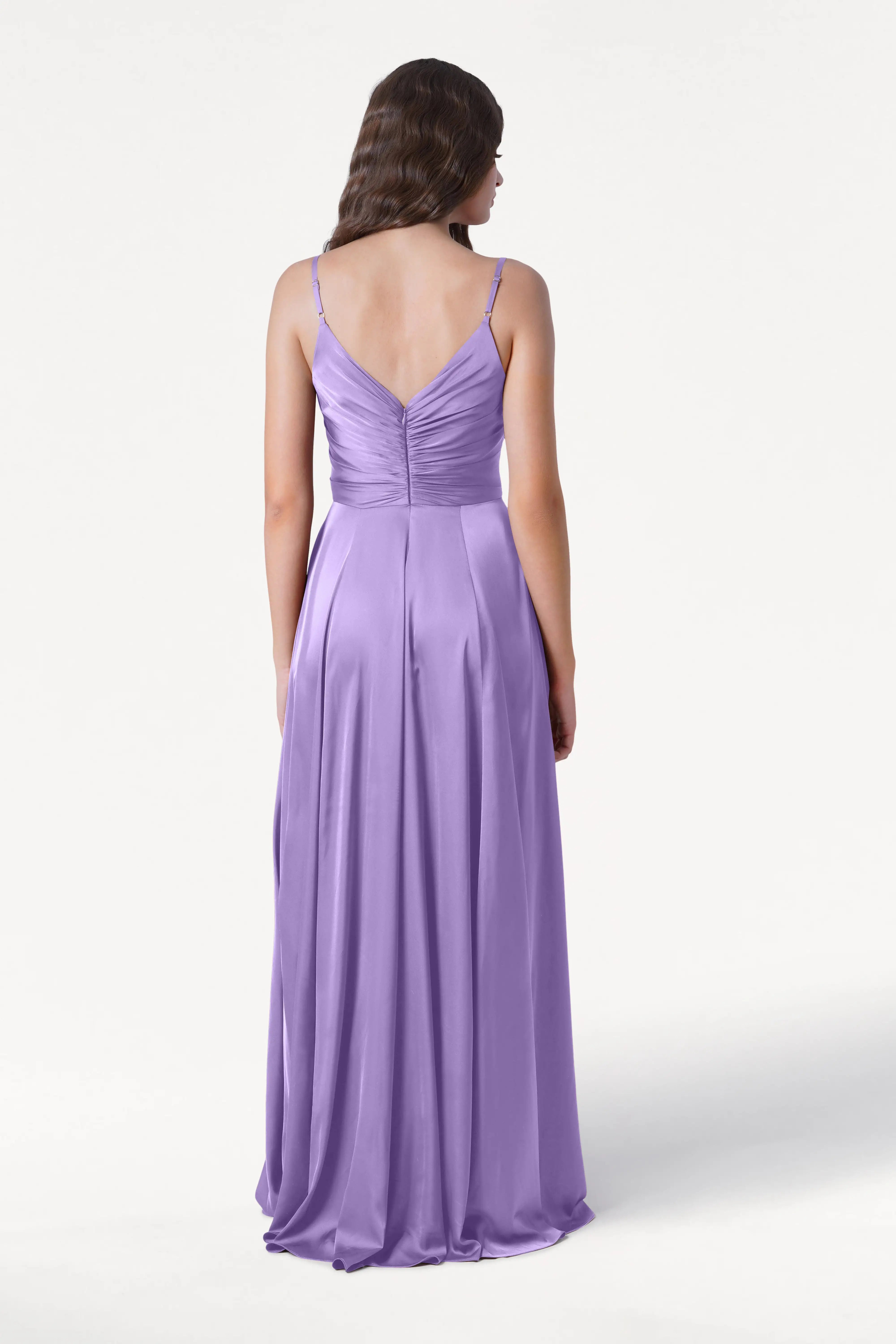 A woman faces away, wearing the TH&TH Isla Bridesmaid Dress in violet satin—featuring thin straps, a pleated bodice, ruched back, and long flowing silhouette—against a plain white background.