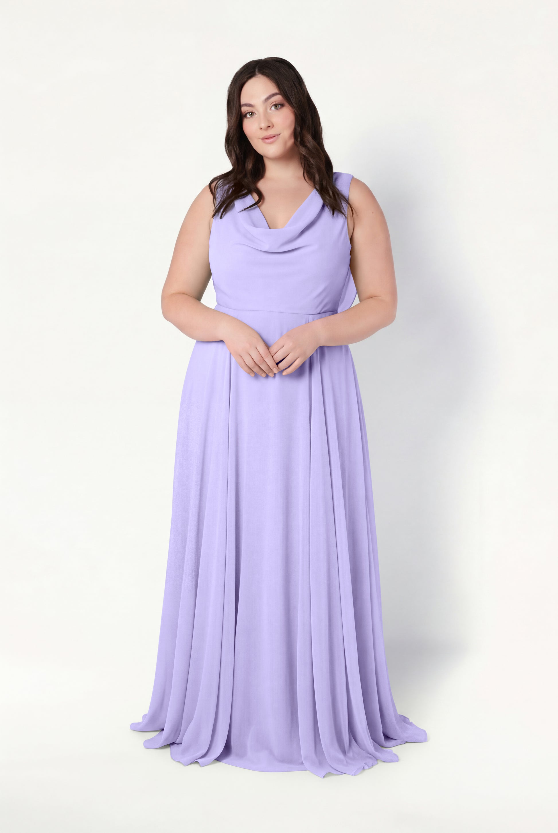 A woman with long brown hair stands against a light background, wearing the TH&TH Athena Bridesmaid Dress in Lilac Mist chiffon, featuring a draped cowl neck. She has a neutral expression and her hands are gently clasped in front of her.