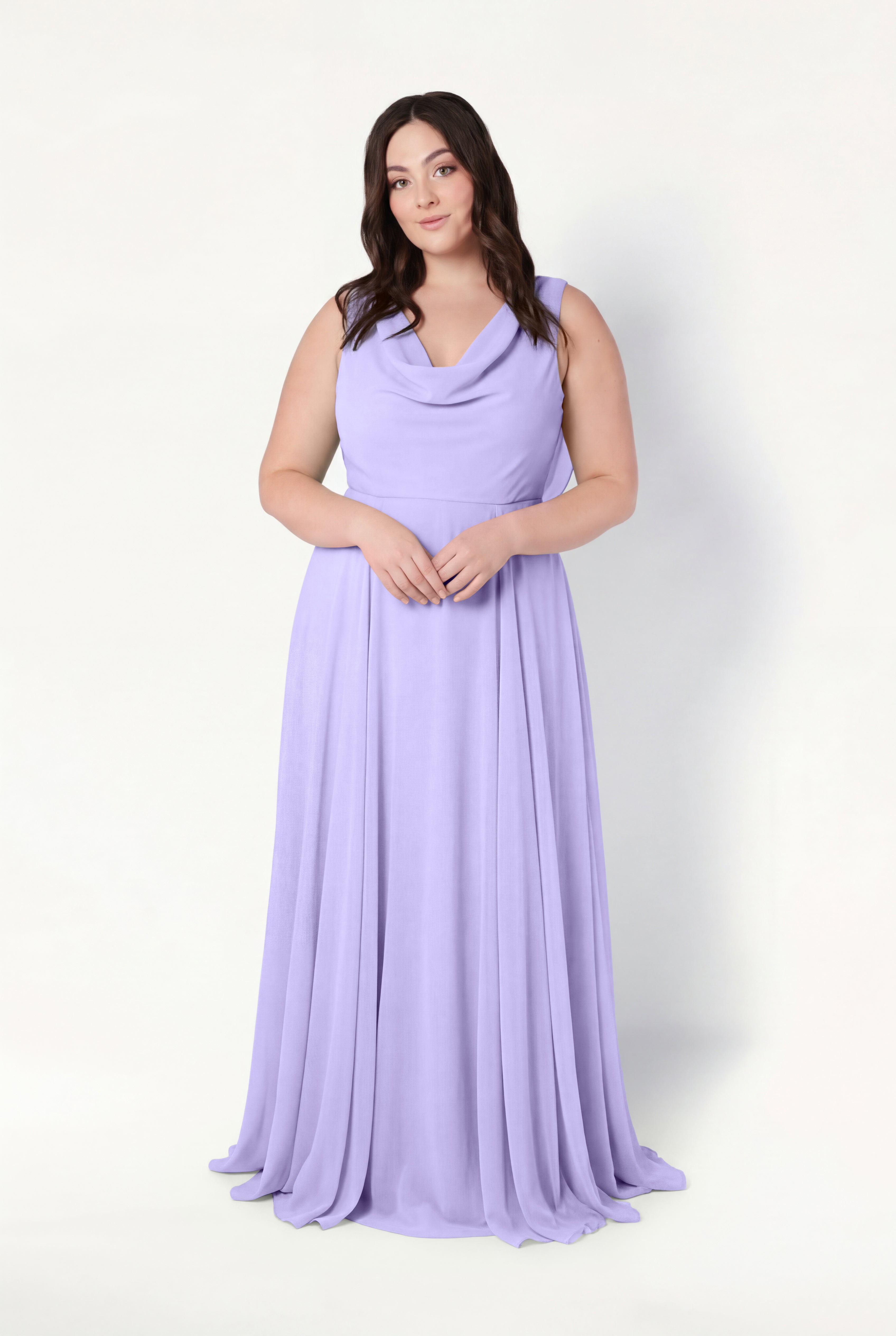 A woman with long brown hair stands against a light background, wearing the TH&TH Athena Bridesmaid Dress in Lilac Mist chiffon, featuring a draped cowl neck. She has a neutral expression and her hands are gently clasped in front of her.