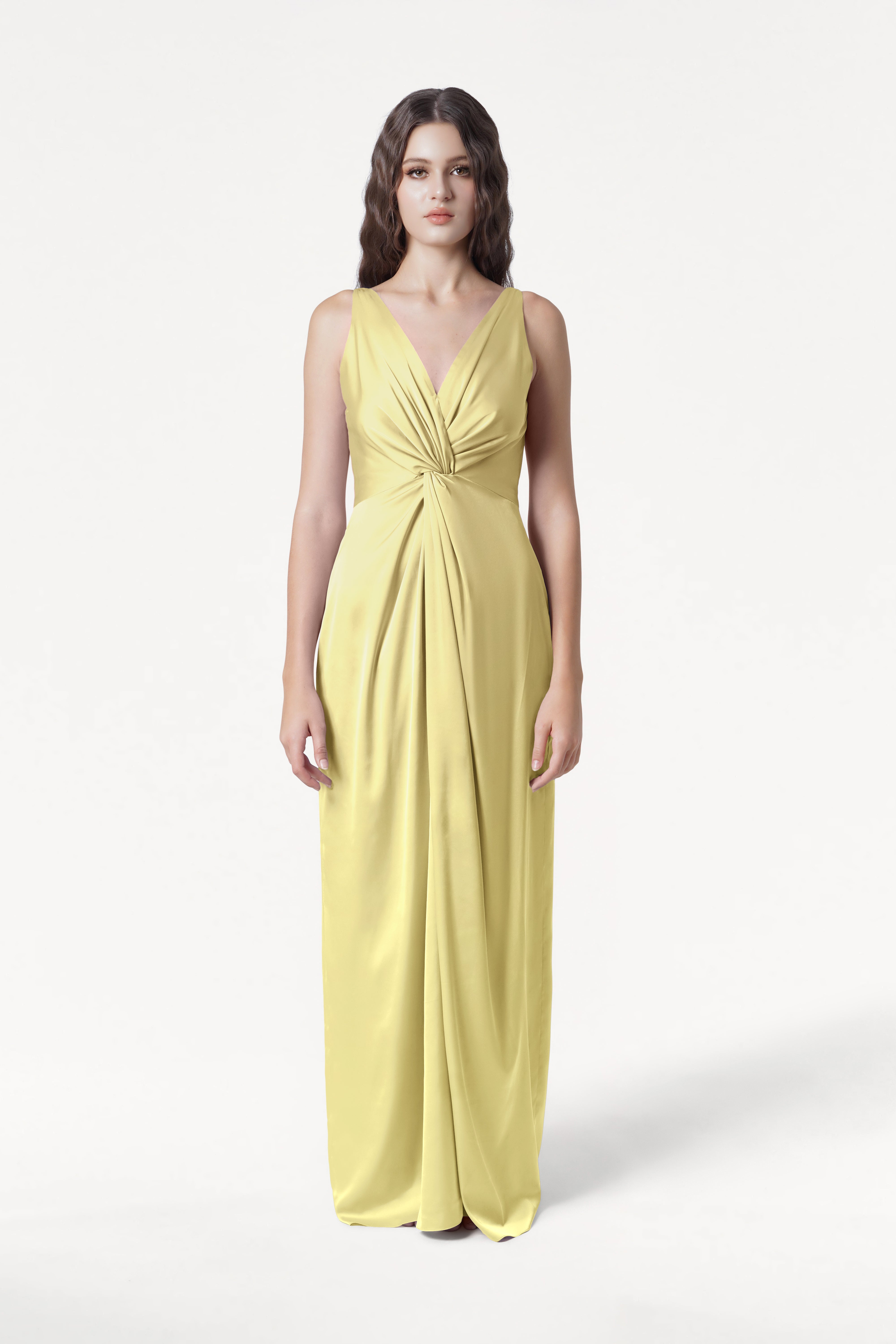 A woman faces forward in the TH&TH Carmen Bridesmaid Dress in Limoncello Satin, a sleeveless, floor-length gown with deep V-neckline and twist-knot waist detail—ideal for modern bridal parties—set against a plain white background.