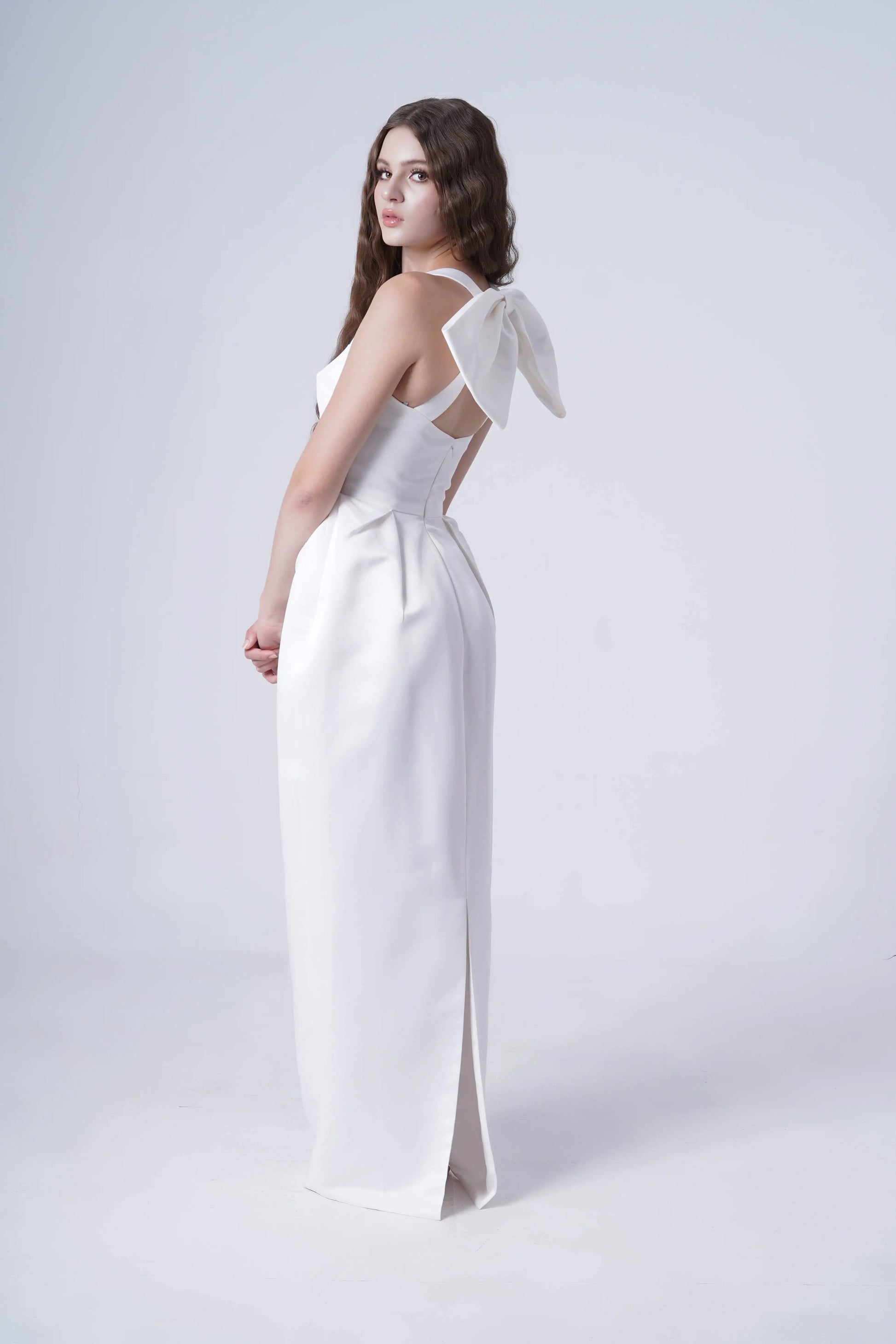 Woman wearing a white dress with bow straps on a plain background