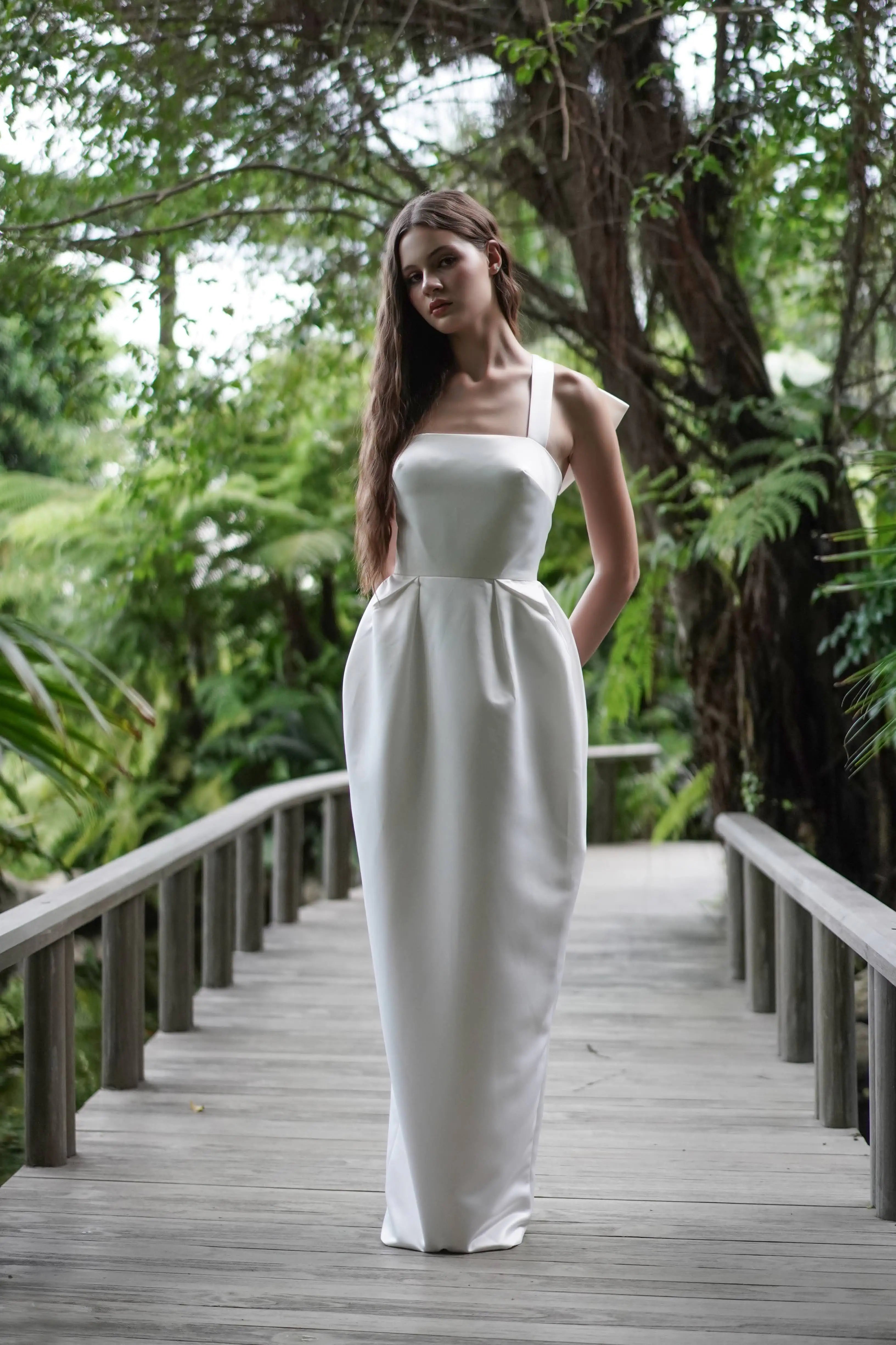 Woman in a white dress standing on a wooden bridge with greenery in the background